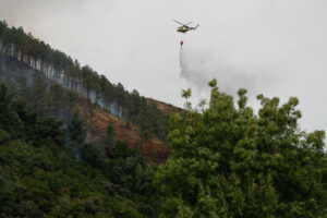 Un helicóptero realiza labores de enfriamiento del terreno, este miércoles en una zona montañosa de Augasmestas, en Quiroga (Lugo). EFE/ Eliseo Trigo