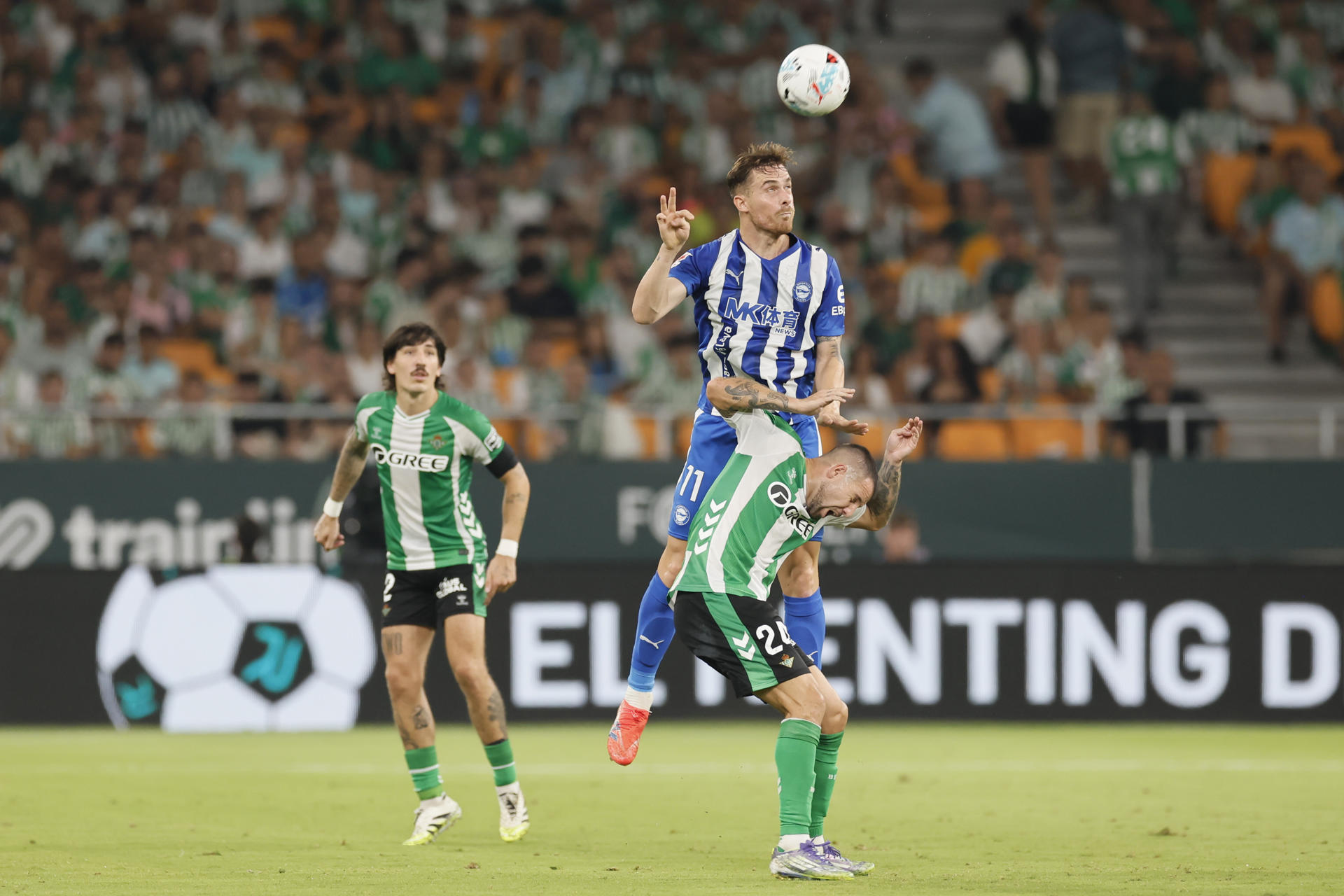 El delantero del Alavés Toni Martín (2d) remata de cabeza ante el centrocampista del Betis Aitor Ruibal (d) durante el partido de LaLiga EA Sports entre el Real Betis y el Alavés, este viernes en el estadio de la Cartuja. EFE/ José Manuel Vidal