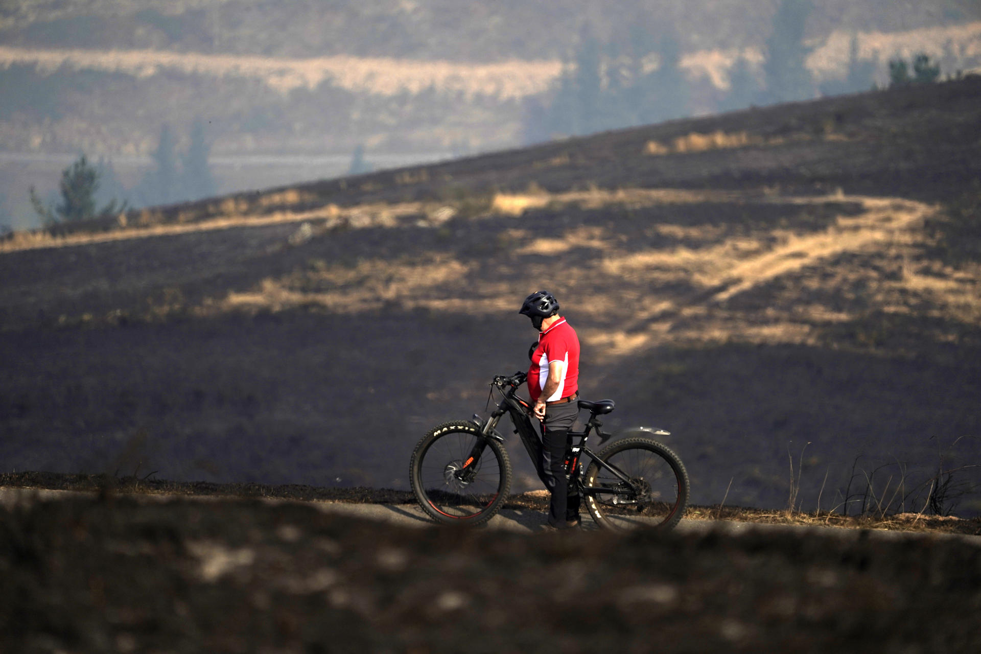 Una persona circula en bicicleta por la zona quemada en las proximidades del Santuario de la Virgen del Acebo este miércoles en Asturias,. Nueve incendios continúan activos esta mañana en Asturias, tres de ellos en el concejo de Cangas del Narcea, donde se concentra el mayor operativo de lucha contra el fuego y donde se ha instalado un Puesto de Mando Avanzado desde el que se sigue la evolución del fuego, que también afecta a los concejos de Allande, Cabrales, Caso, Coaña y Ponga. EFE/Paco Paredes
