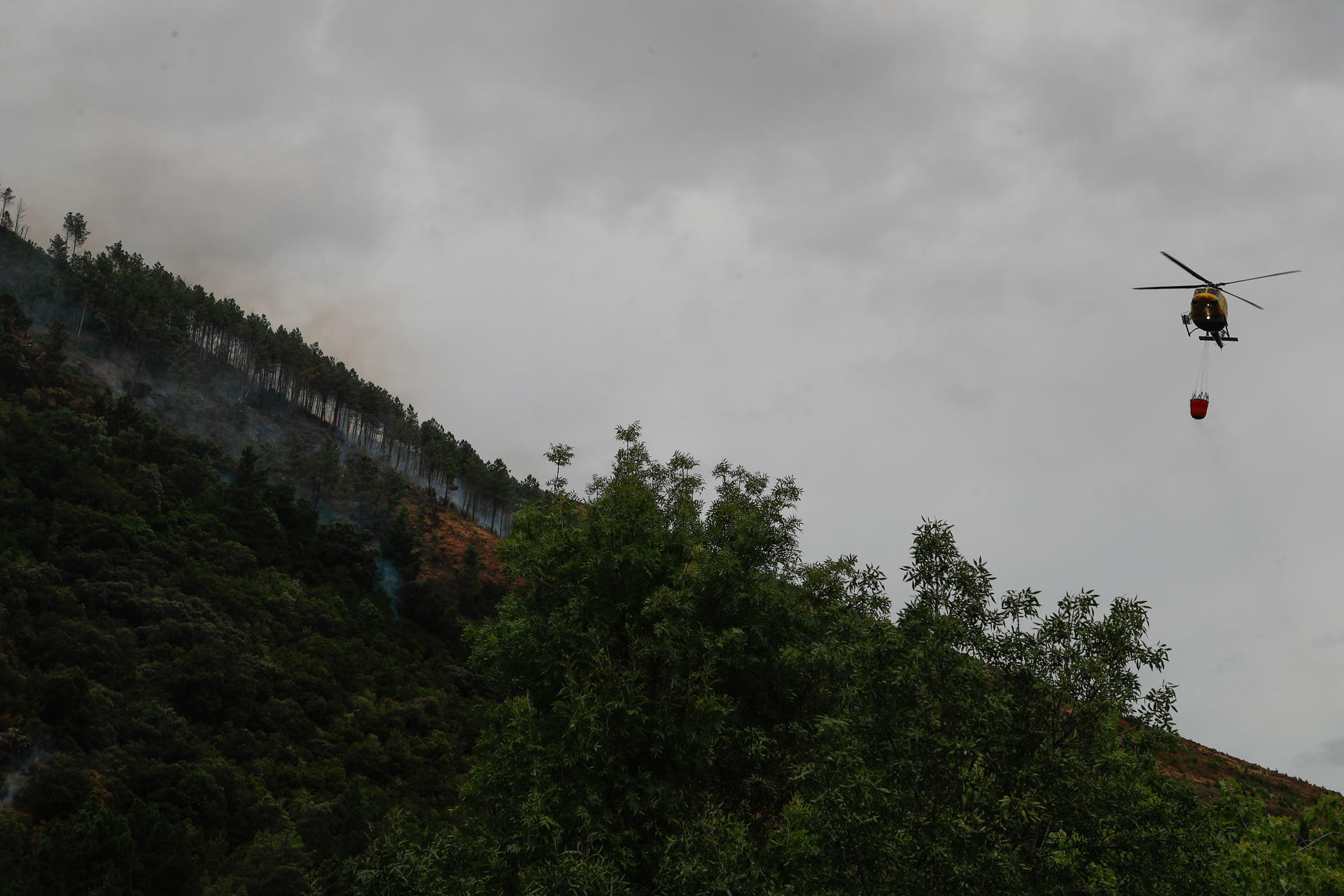 Un helicóptero realiza labores de enfriamiento del terreno, este miércoles en una zona montañosa de Augasmestas, en Quiroga (Lugo). EFE/Eliseo Trigo