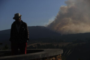 Un hombre camina con la columna de humo de fondo desde el Mirador da Capela en Pobra de Brollón, Lugo. EFE/ Eliseo Trigo