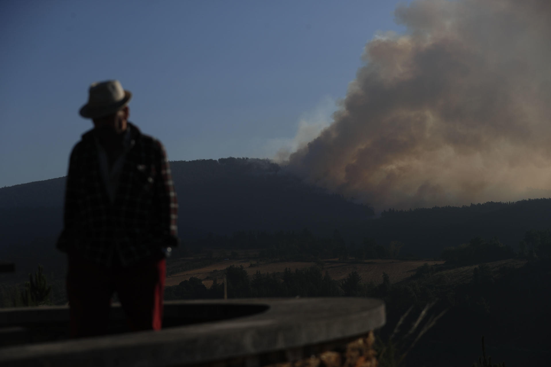 Un hombre camina con la columna de humo de fondo desde el Mirador da Capela en Pobra de Brollón, Lugo. EFE/ Eliseo Trigo