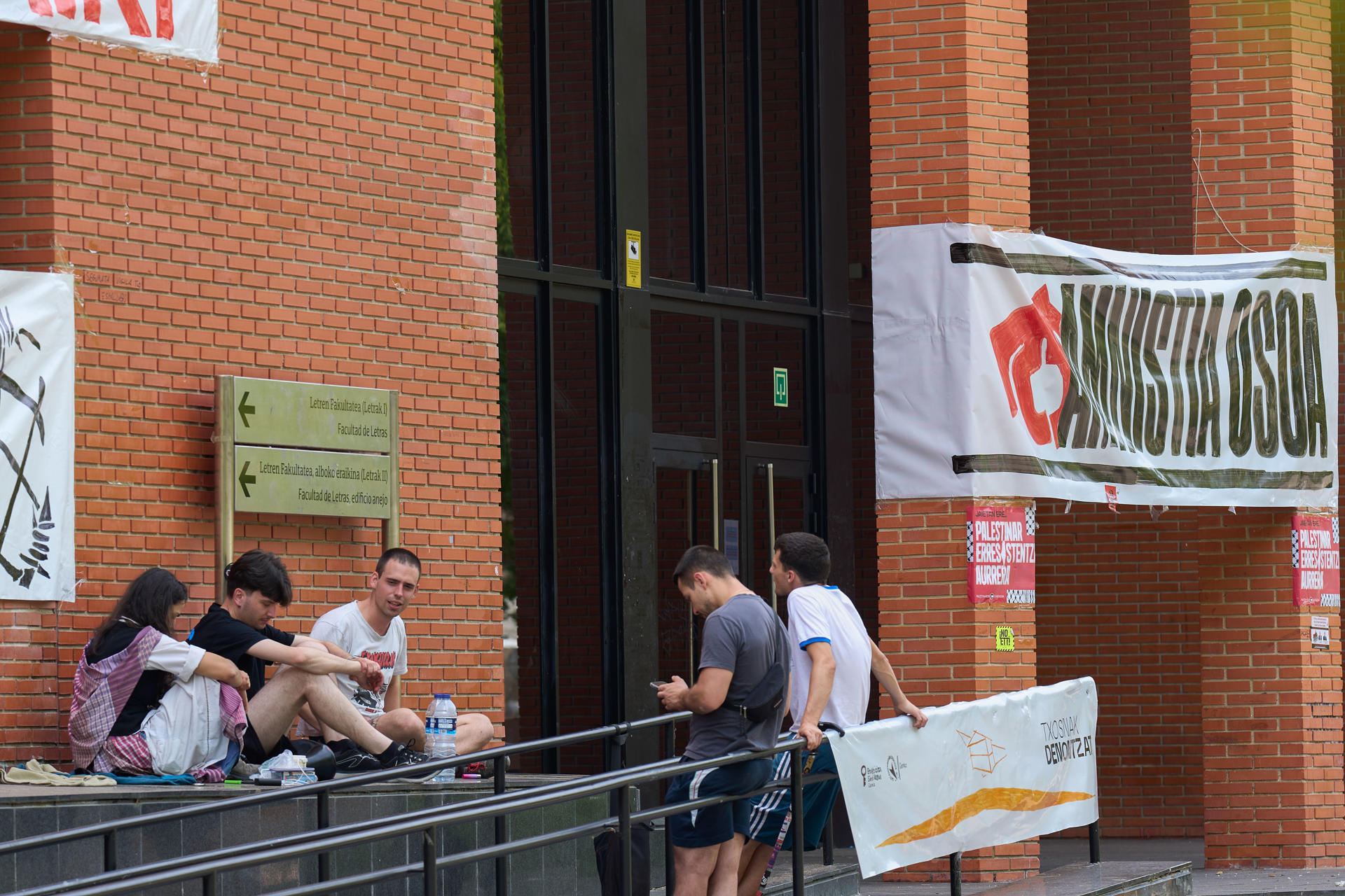 Varios jóvenes sentados en la entrada de la Facultad de Letras de Vitoria, donde esta el recinto de las fiestas de la capital vasca con un cartel que pide la amnistía de los presos de ETA. EFE/ Adrian Ruiz Hierro