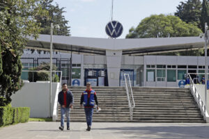 Dos personas caminan frente a la fachada de la planta armadora Volkswagen, en el estado de Puebla (México). Imagen de archivo. EFE/Hilda Ríos