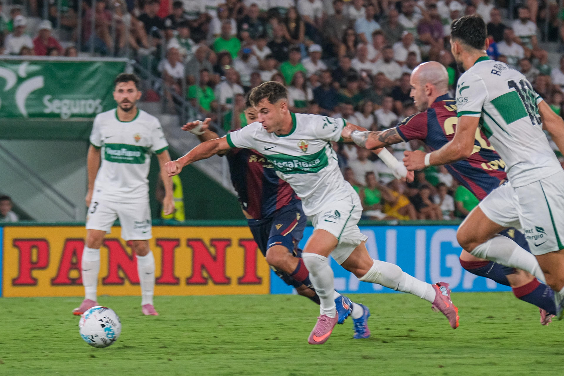 El centrocampista del Elche Germán Valera (c) pelea un balón con dos rivales del Levante durante el partido de la tercera jornada de LaLiga EA Sports en el estadio Martínez Valero. EFE/Pablo Miranzo