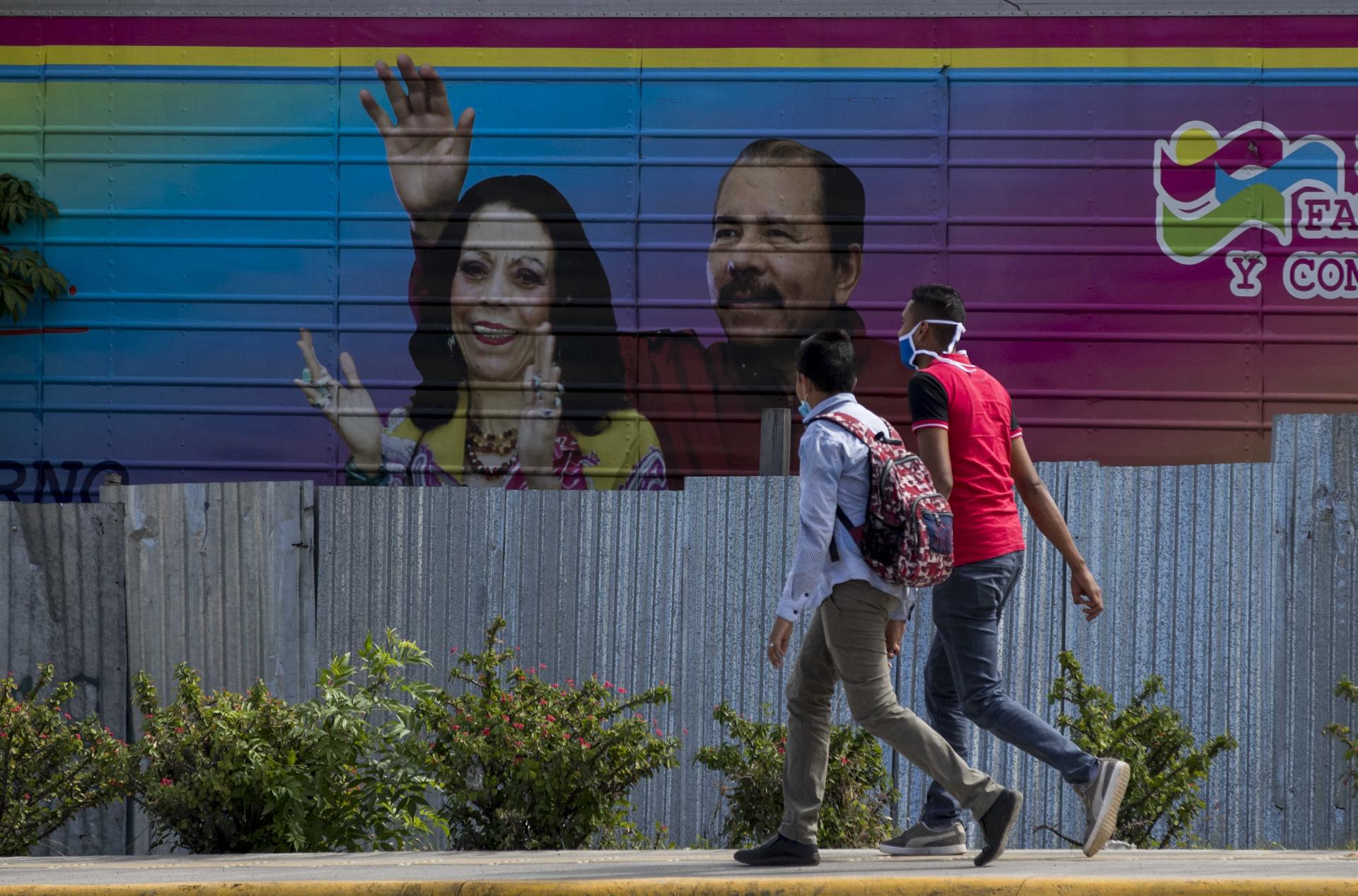 Fotografía de archivo de un par de jóvenes al caminar frente a una pancarta con la imagen del presidente de Nicaragua, Daniel Ortega (d), y su esposa y copresidenta, Rosario Murillo (i), en Managua (Nicaragua). EFE/Str