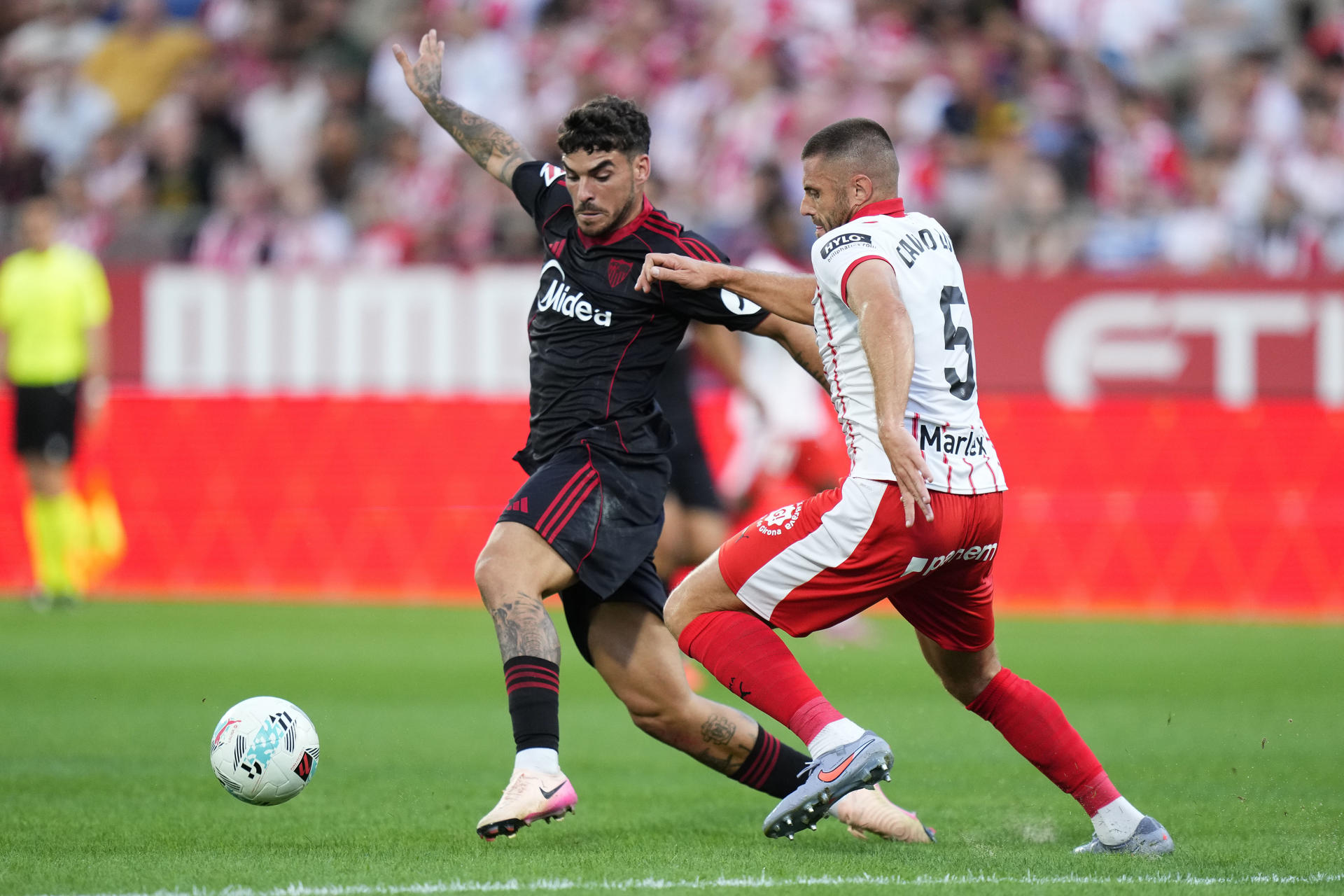 El defensa del Girona David López (d) lucha con Isaac Romero, del Sevilla, durante el partido de la tercera jornada de LaLiga que Girona FC y Sevilla FC disputan este sábado en el estadio Municipal de Montilivi. EFE/Siu Wu