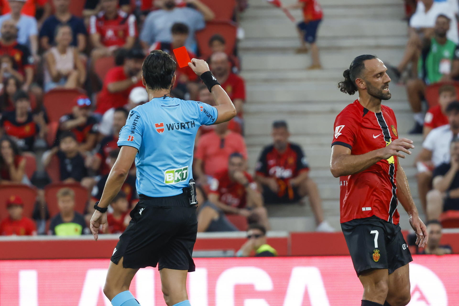 El árbitro del encuentro José Luis Munuera (i) saca tarjeta roja a Vedat Muriqi (d) del Mallorca este sábado, durante la primera jornada de LaLiga EA Sports, entre el RCD Mallorca y el FC Barcelona, en el estadio de Son Moix de Palma de Mallorca. EFE/ Cati Cladera
