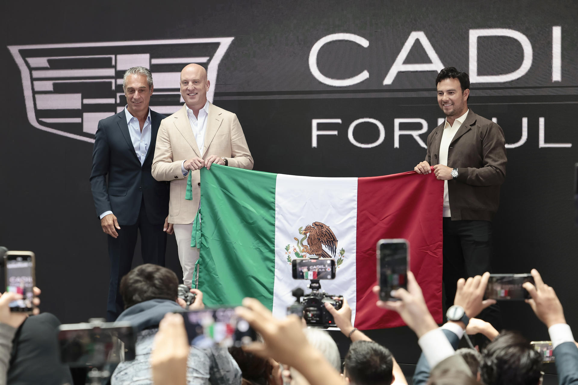 El piloto mexicano, Sergio Pérez (d); el director ejecutivo de Cadillac, Dan Towriss (c), y el presidente del Consejo de Administración de Grupo Carso, Carlos Slim Domit (i), posan con una bandera de México este miércoles, en Ciudad de México (México).  EFE/José Méndez