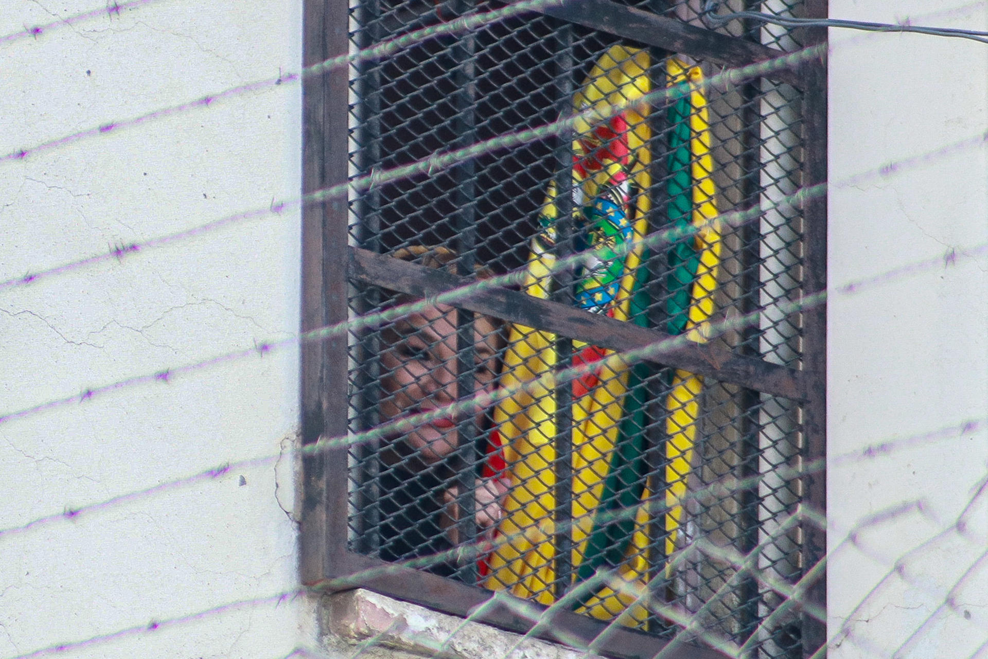 La expresidenta interina de Bolivia Jeanine Áñez sostiene una bandera de Bolivia desde una ventana este lunes, en el Centro de Orientación Femenina de Miraflores, en La Paz (Bolivia). EFE/ Gabriel Márquez