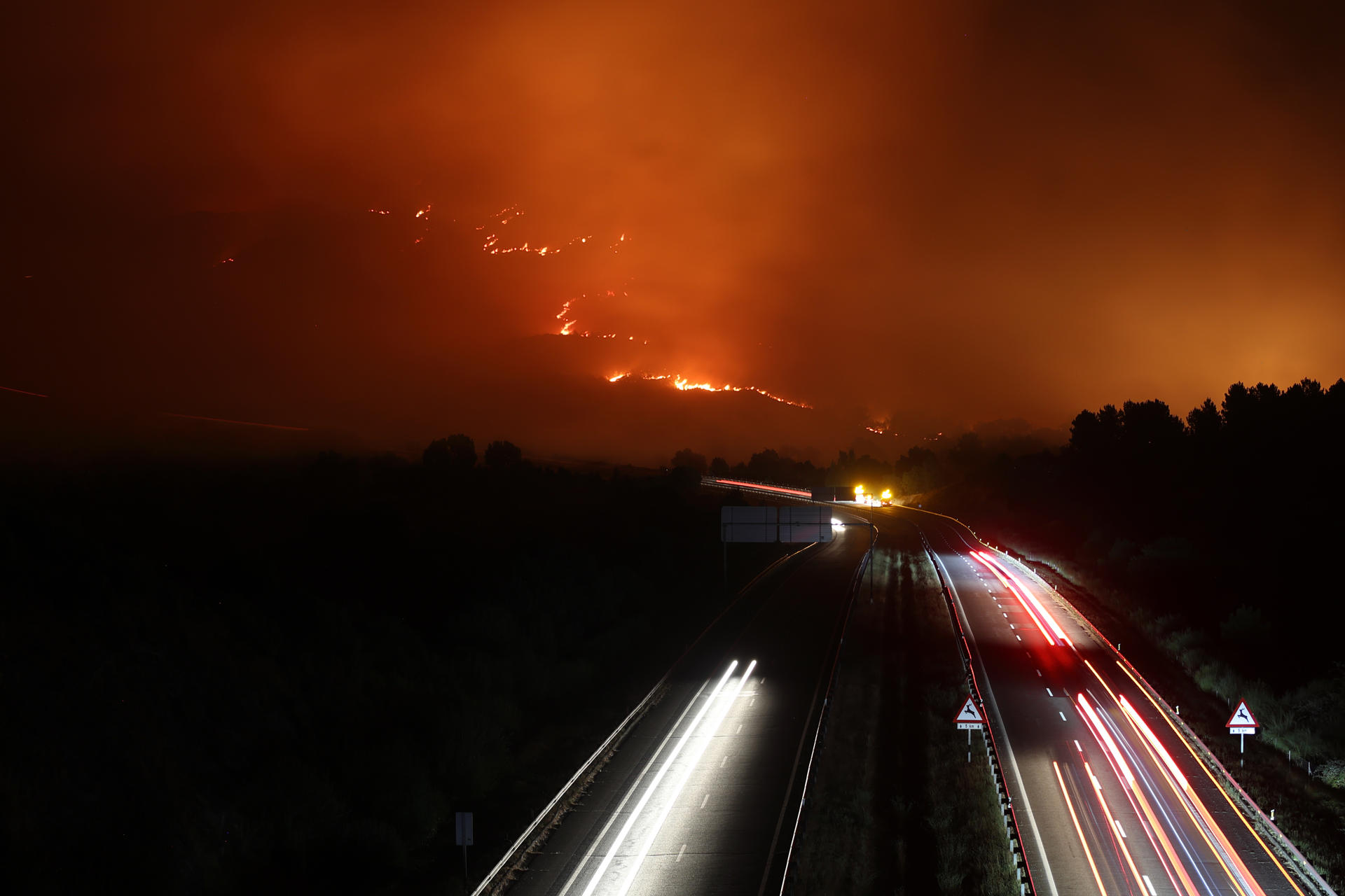 Vista de la A-52 en la madrugada de este domingo, en Orense (Galicia) con un incendio cercano a la carretera. Trece carreteras españolas, dos de ellas nacionales, continúan cortadas en la mañana de este domingo a causa de los incendios forestales que afectan a varias provincias de Asturias, Castilla y León, Extremadura y Galicia, ha informado la Dirección General de Tráfico (DGT). EFE/ Sxenick