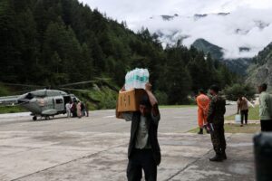 Un hombre lleva botellas de agua mientras un helicóptero de la Fuerza Aérea India que transportaba materiales de socorro opera durante la misión de rescate en Harshil, después del aguacero en la aldea de Dharali en el distrito de Uttarkashi, estado de Uttarakhand, norte de la India, el 14 de agosto. EFE/EPA/RAJAT GUPTA