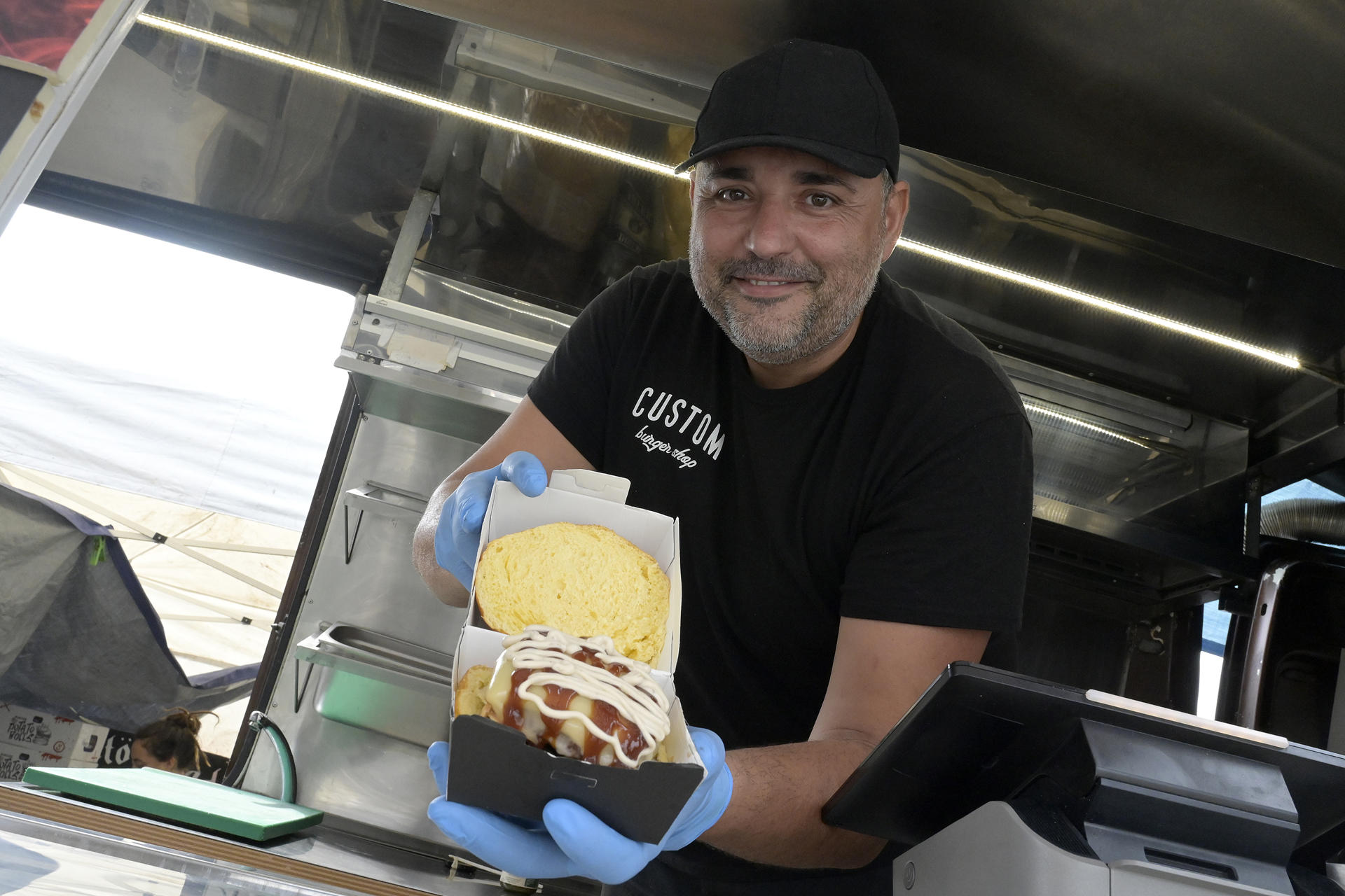 A CORUÑA, 23/08/2025.- Yonathan Martínez muestra la Food Truck "CUSTOM BURGUER". Inspiración americana con producto gallego son las ideas que triunfan en el campeonato de hamburguesas The Champions Burger, que supera su ecuador hacia la final de diciembre. Tras visitar más de una veintena de ciudades, The Champions Burguer está en A Coruña, de forma simultánea a Torrevieja (Alicante), Gandía (Valencia) y Mijas (Málaga) -estas dos últimas con diferentes formatos- y se prepara para abrir en Vigo la próxima semana, además de otra veintena de citas pendientes a partir de septiembre, hasta un total de cincuenta ciudades. Entre los más de veinte restaurantes que participan, tienen una gran acogida las ofertas de Carnivale (A Coruña), Custom Burger y Malasogra (ambos de Santiago y su área). EFE/Moncho Fuentes