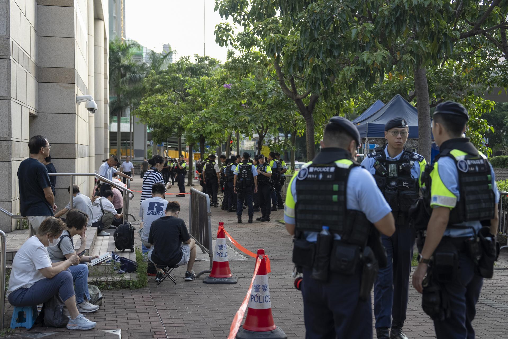 Agentes de policía hacen guardia junto a personas que esperan en fila afuera de los Tribunales de Magistrados de West Kowloon antes de la reanudación de los argumentos finales del juicio por seguridad nacional de Jimmy Lai en Hong Kong, China, el 27 de agosto de 2025. EFE/EPA/Leung Man Hei