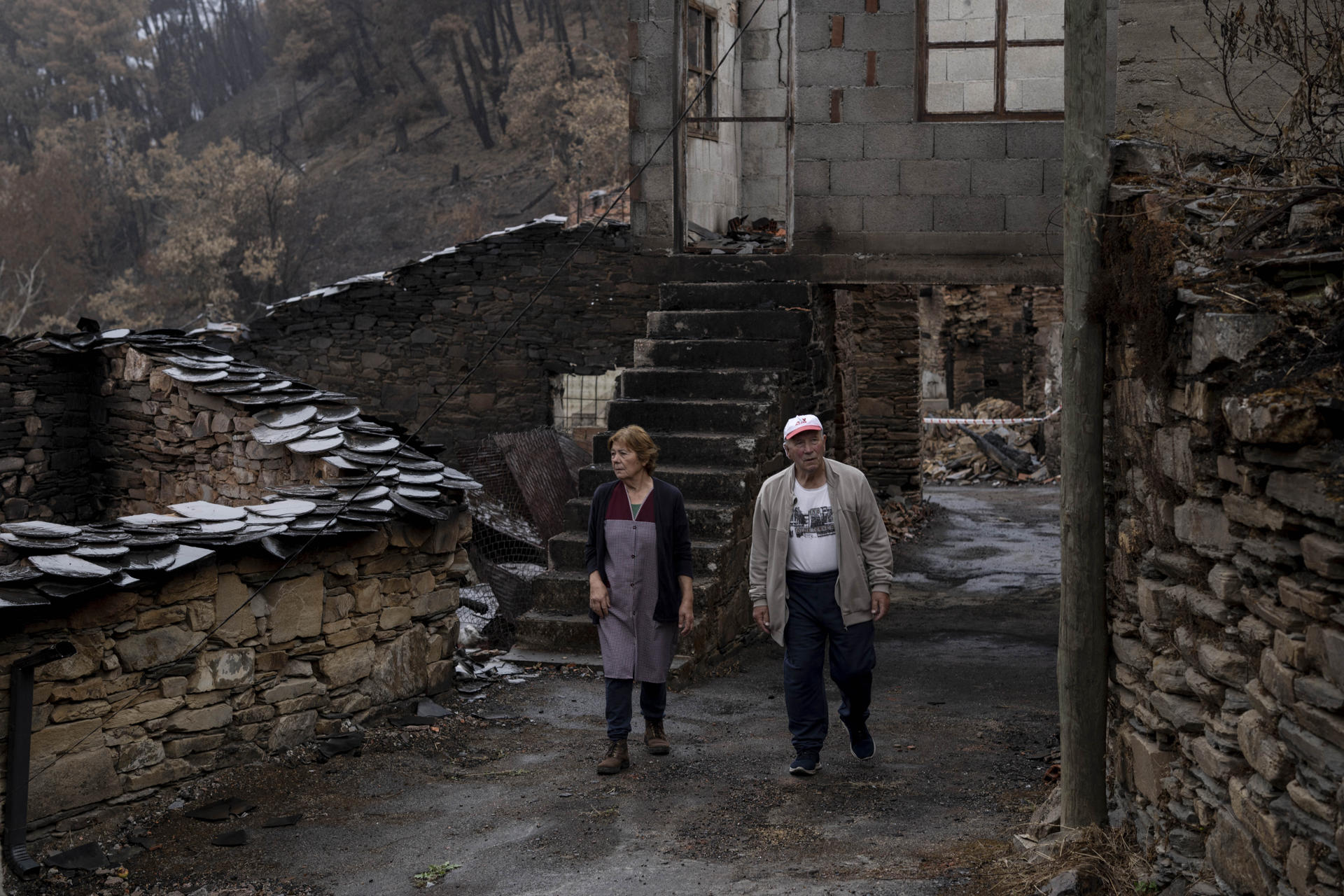 Ana Sánchez y Leopoldo Nogueira, matrimonio y vecinos de San Vicente de Leira, caminan entre las viviendas quemadas en dicha localidad, en Vilamartín de Valdeorras (Ourense). Se cumple un mes del mayor incendio de la historia de Galicia, el que se originó en Larouco (Ourense) el pasado 13 de agosto y que calcinó más de 30.000 hectáreas. Los daños son aún visibles y los vecinos recuerdan con estupor lo sucedido mientras afrontan con desesperanza la reconstrucción. EFE/Brais Lorenzo
