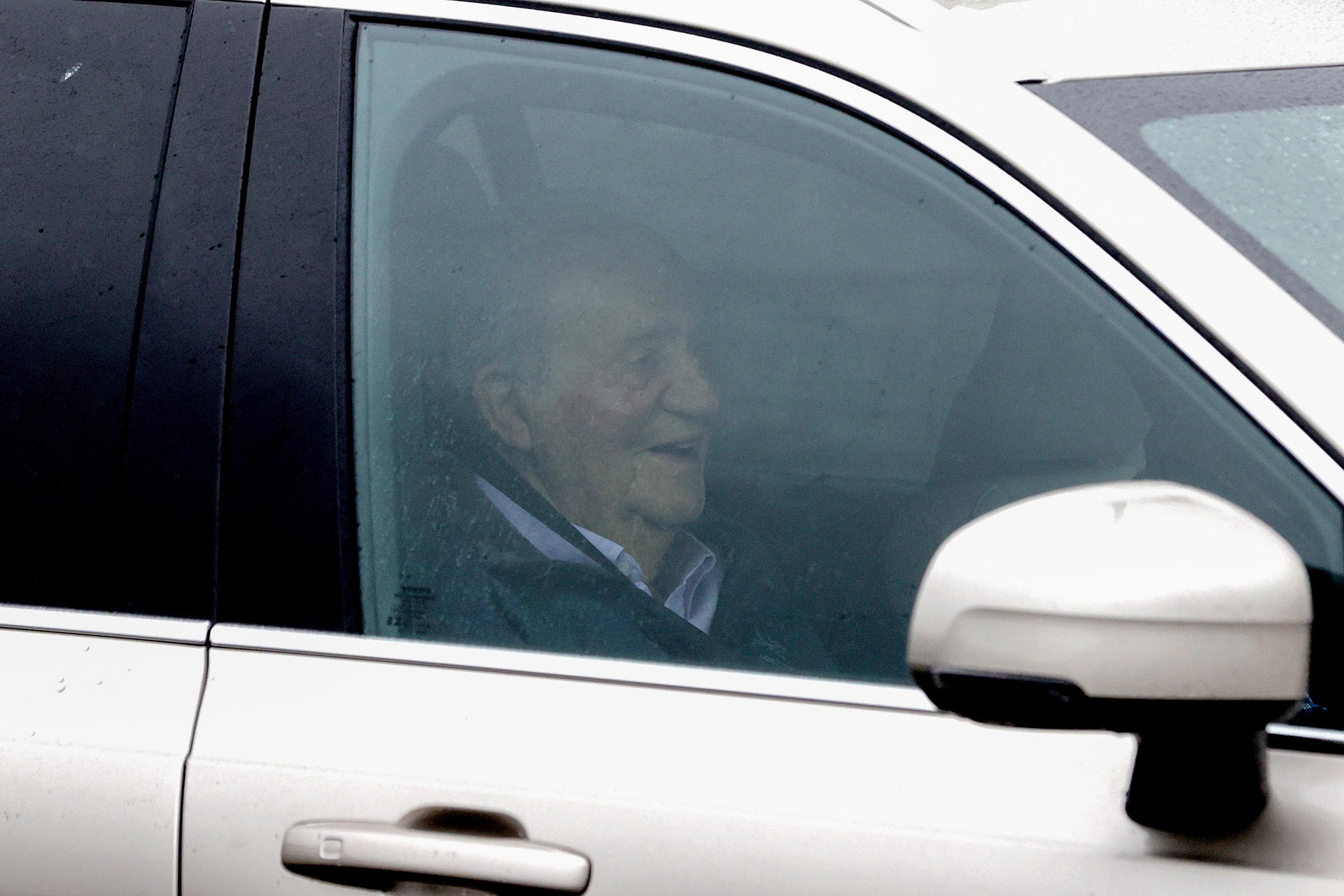 El rey emérito Juan Carlos I sonríe a bordo de un vehículo a su llegada este jueves al aeropuerto de A Coruña, donde fue por su amigo Pedro Campos, antes de dirigirse a Sanxenxo para participar en la décima edición de la regata que lleva su nombre, última prueba de preparación para el Mundial de la clase 6 metros que se disputará a partir del 22 de septiembre en el Seawanhaka Corinthian Yacht Club, en Nueva York. EFE/ Cabalar