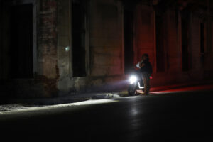 Fotografía de archivo de una pareja al conversar en medio de una calle en penumbra, iluminada por la luz de una motocicleta, durante uno de los tradicionales cortes eléctricos diarios, en La Habana (Cuba). EFE/Ernesto Mastrascusa