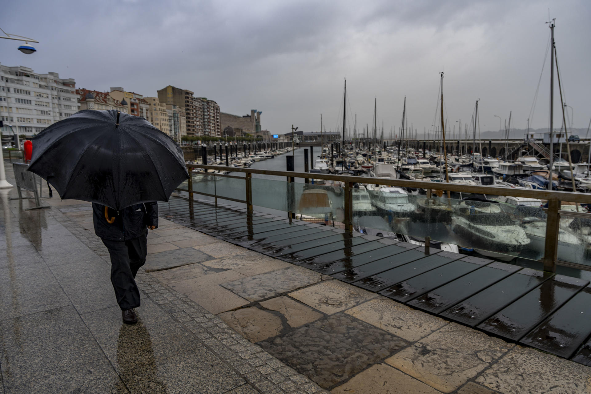Un hombre se protege de la lluvia por el puerto de Santander, este lunes. EFE/Román G. Aguilera