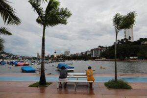 Dos personas permanecen en una banca durante una mañana fría y con ventiscas en el balneario de Acapulco, estado de Guerrero (México). Fotografía de archivo. EFE/ David Guzmán