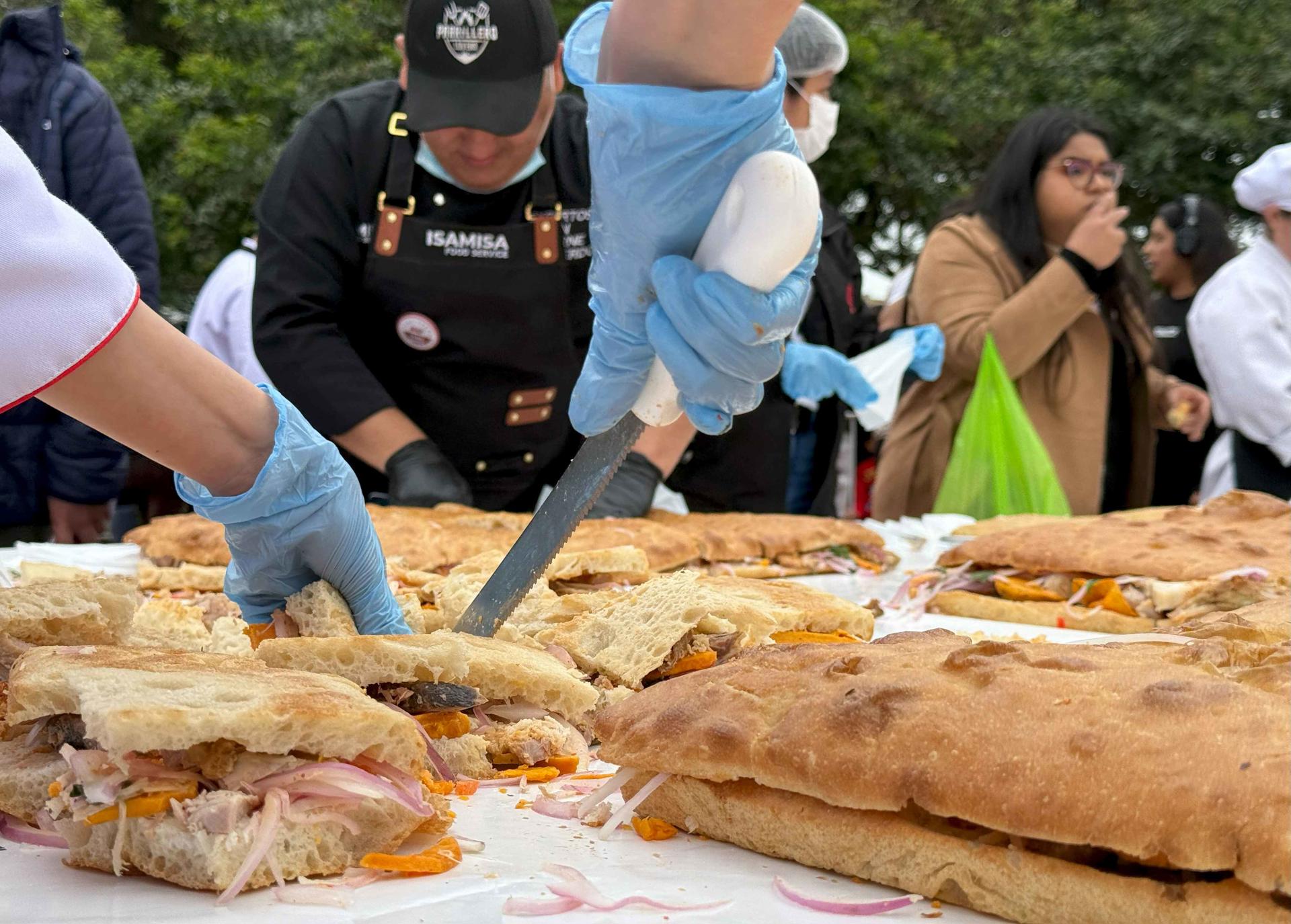 Personas preparan un pan con chicharrón este miércoles, en el distrito de Magdalena del Mar, en Lima (Perú). EFE/ Mikhail Huacán
