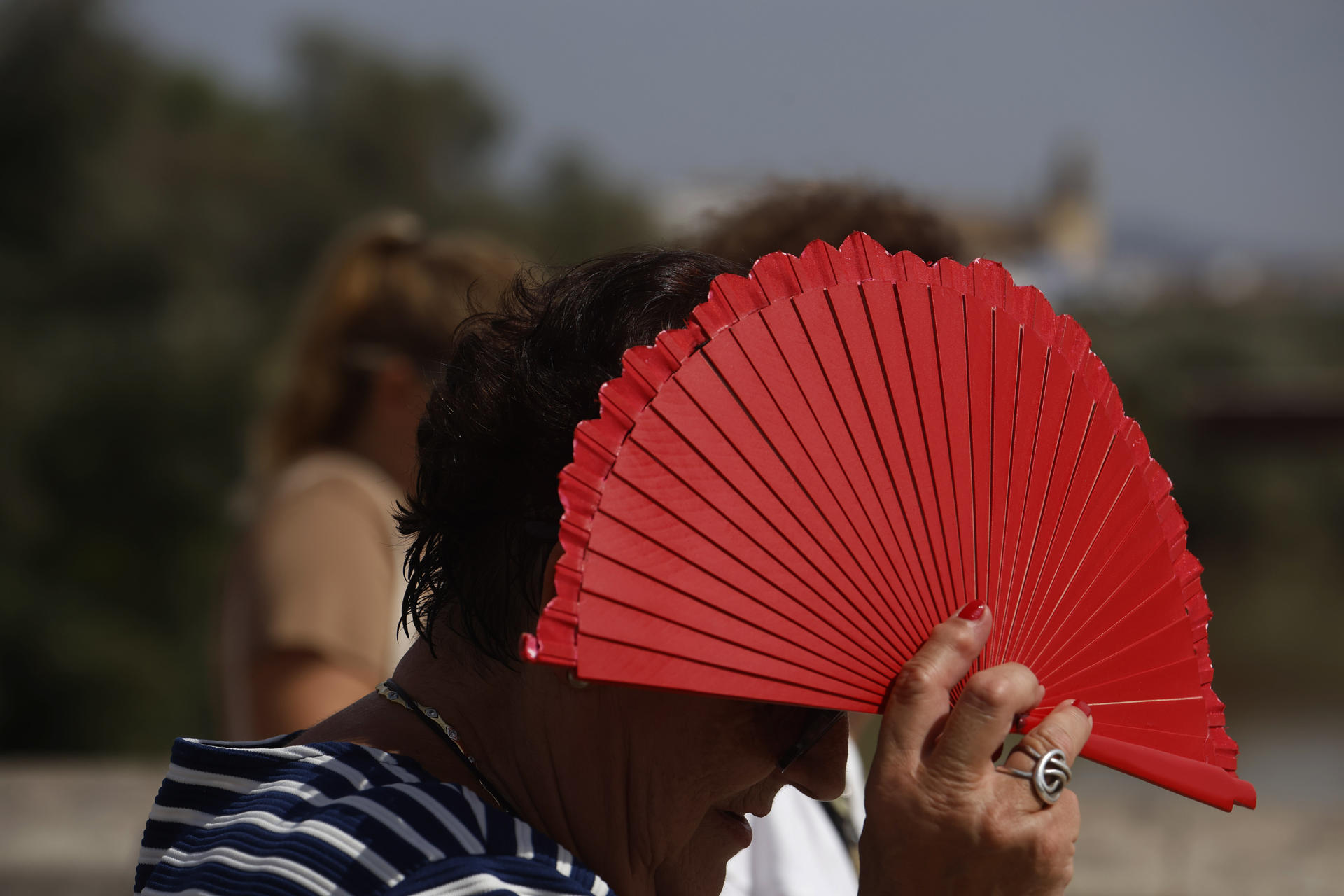 Una mujer intenta resguardarse la cabeza del sol con un abanico mientras camina por el Puente Romano de Córdoba este jueves. EFE/Salas