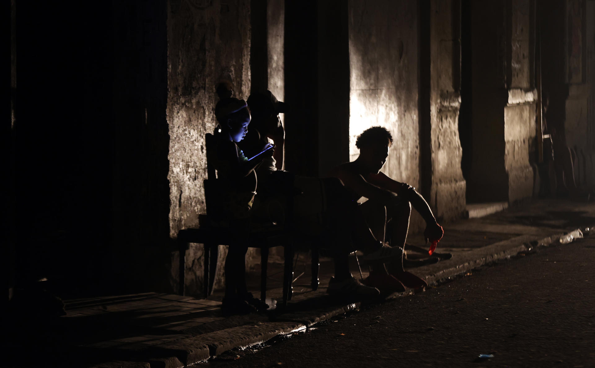 Personas sentadas en la acera de su casa esperan el regreso de la electricidad este miércoles, en La Habana (Cuba). EFE/Ernesto Mastrascusa