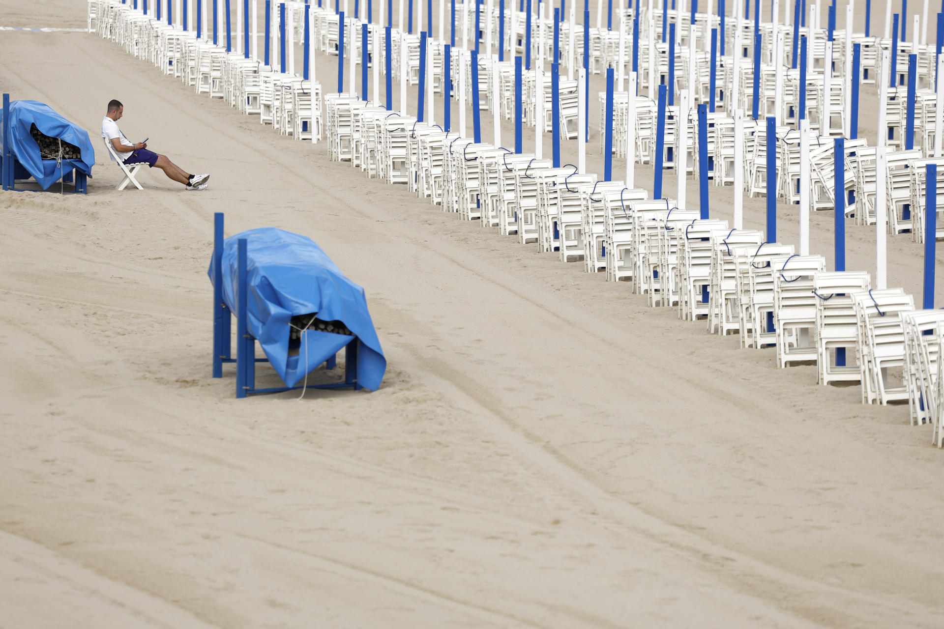 Un toldero espera la llegada de los bañistas este lunes en la playa de la Zurriola de San Sebastián. EFE/Juan Herrero