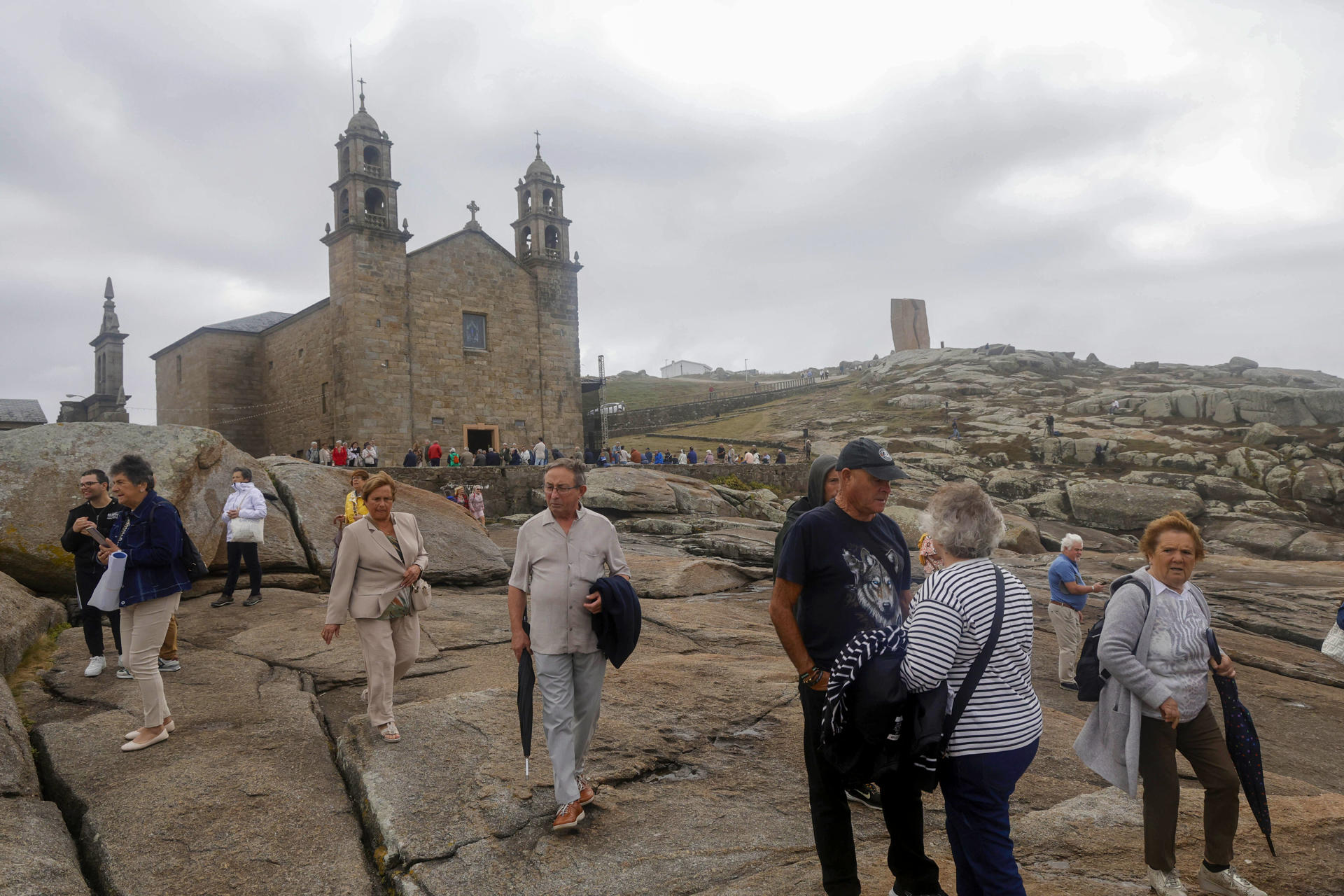 Fieles en las proximidades de la Basílica de la Virge de la Barca asisten a la romería de la Virxe da Barca, que este 2025 ha captado el interés de medios internacionales, este domingo en Muxia. EFE/Kiko Delgado
