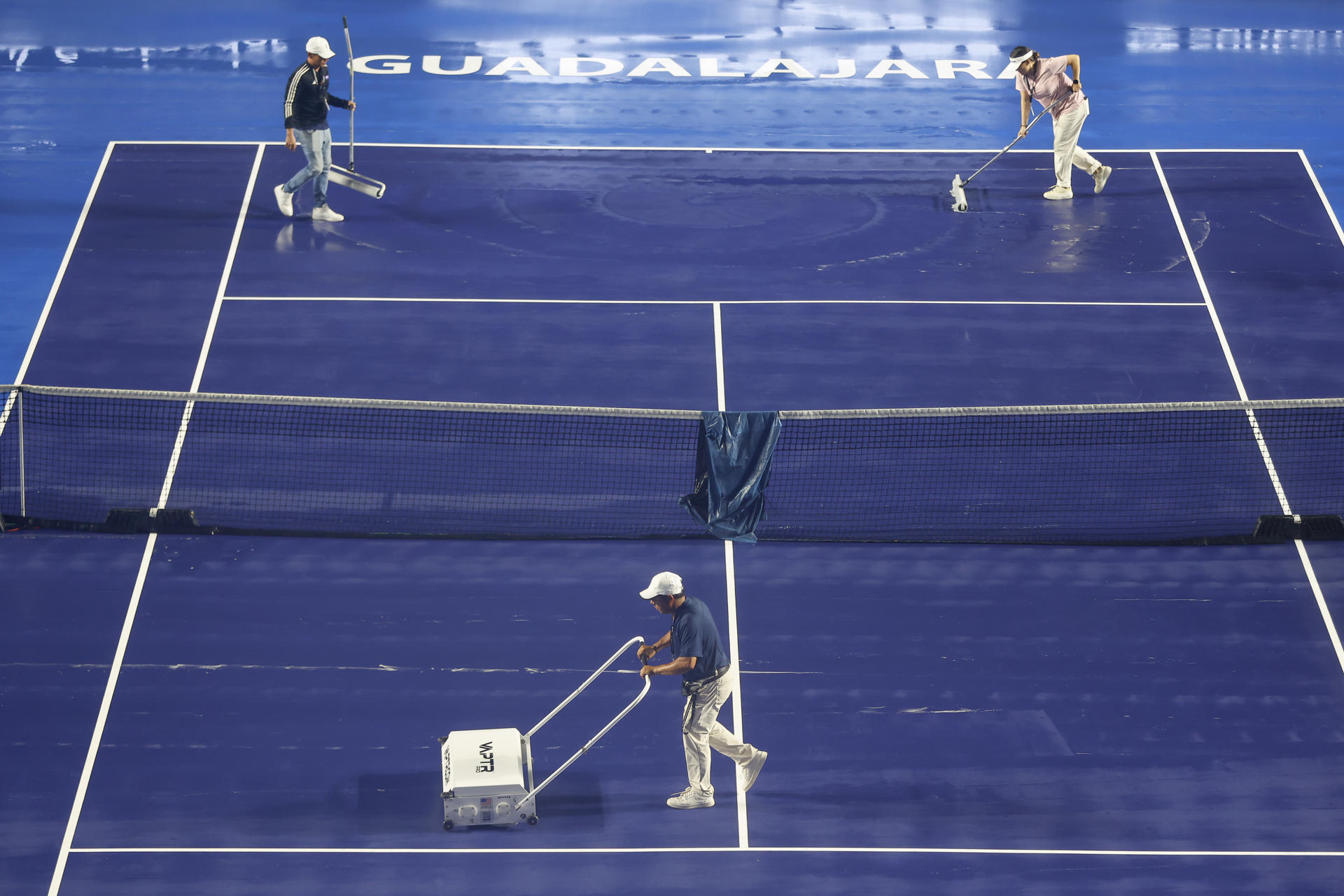 Trabajadores secan la cancha este lunes, previo a reanudar el partido del torneo Guadalajara Open WTA 500 entre la griega Maria Sakkari y la francesa Elsa Jacquemot en el Centro Panamericano de Tenis, en Guadalajara (México). EFE/Francisco Guasco