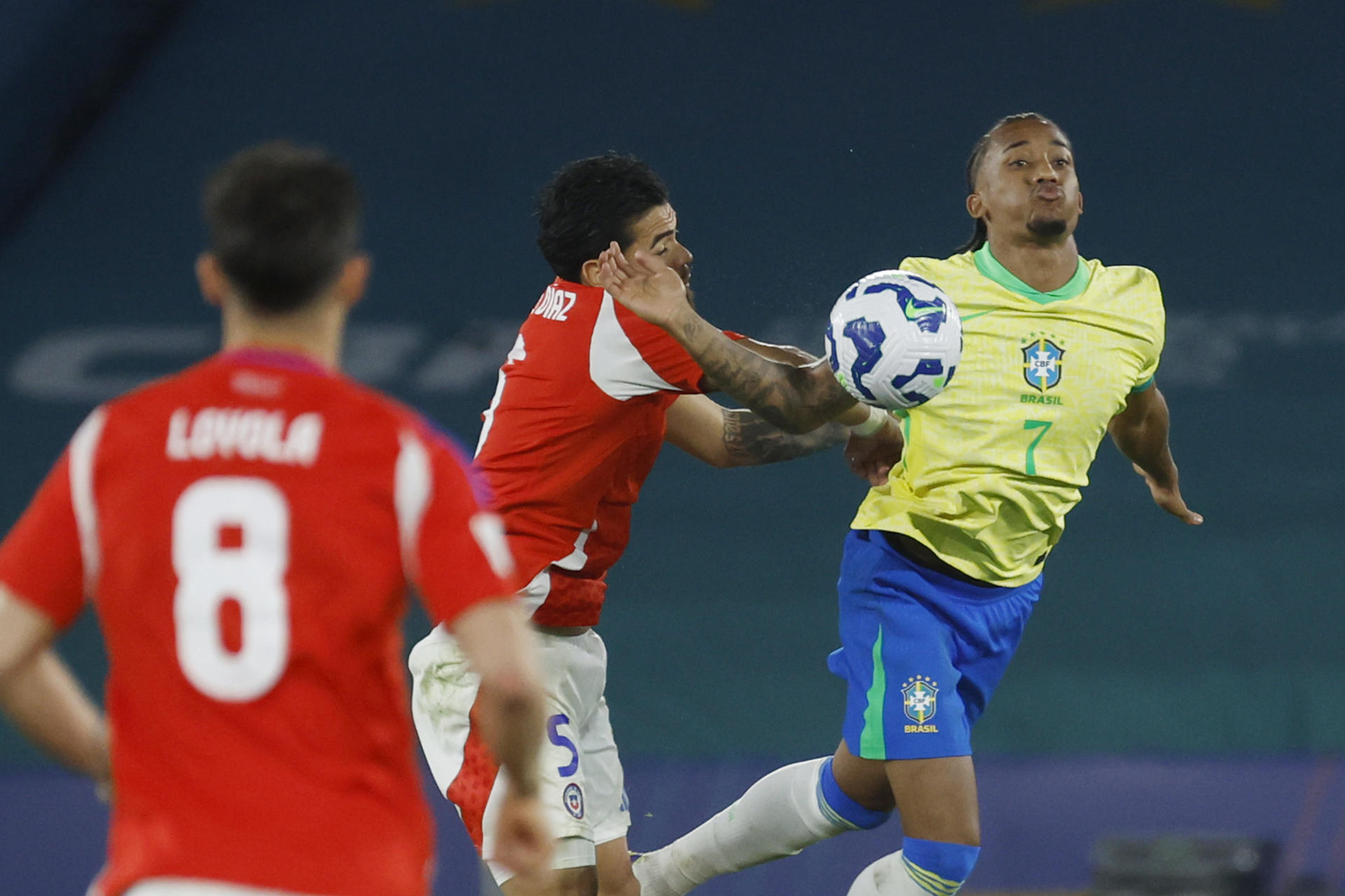 El extremo brasileño João Pedro (d) soporta la presión del defensor chileno Paulo Díaz (c) este jueves durante el partido que la Canarinha ganó por 3-0 en el estadio Maracaná de Río de Janeiro (Brasil). EFE/ Antonio Lacerda