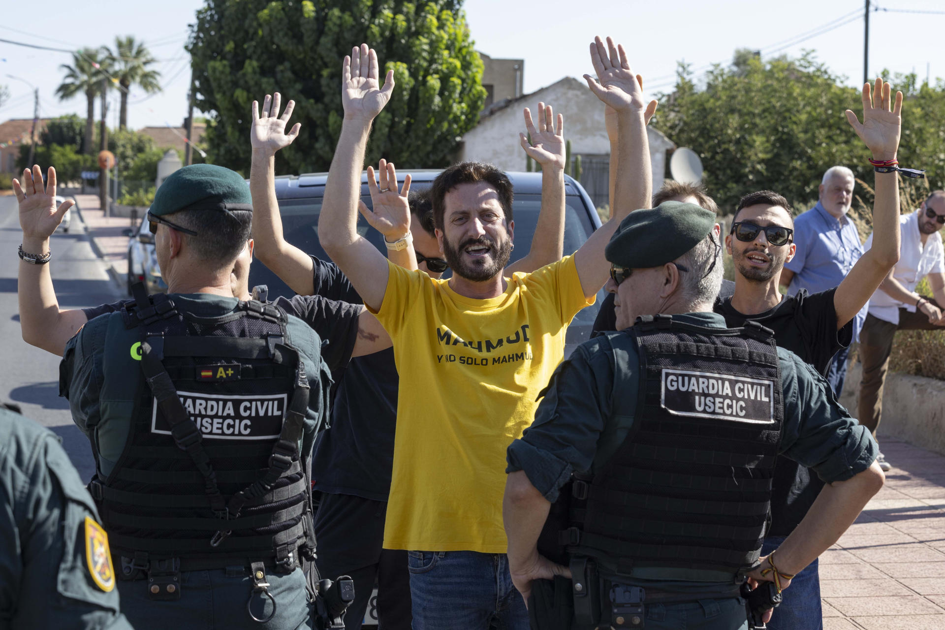 El secretario de comunicación de Podemos en Murcia Víctor Egío (c), acompañado por otros miembros del partido protestan durante la rueda de prensa que ha ofrecido el portavoz nacional de VOX de Inmigración, Interior y seguridad Samuel Vázquez, este miércoles junto al centro de menas de Santa Cruz, que estaba acordonado por agentes de la guardia civil. EFE/Marcial Guillén