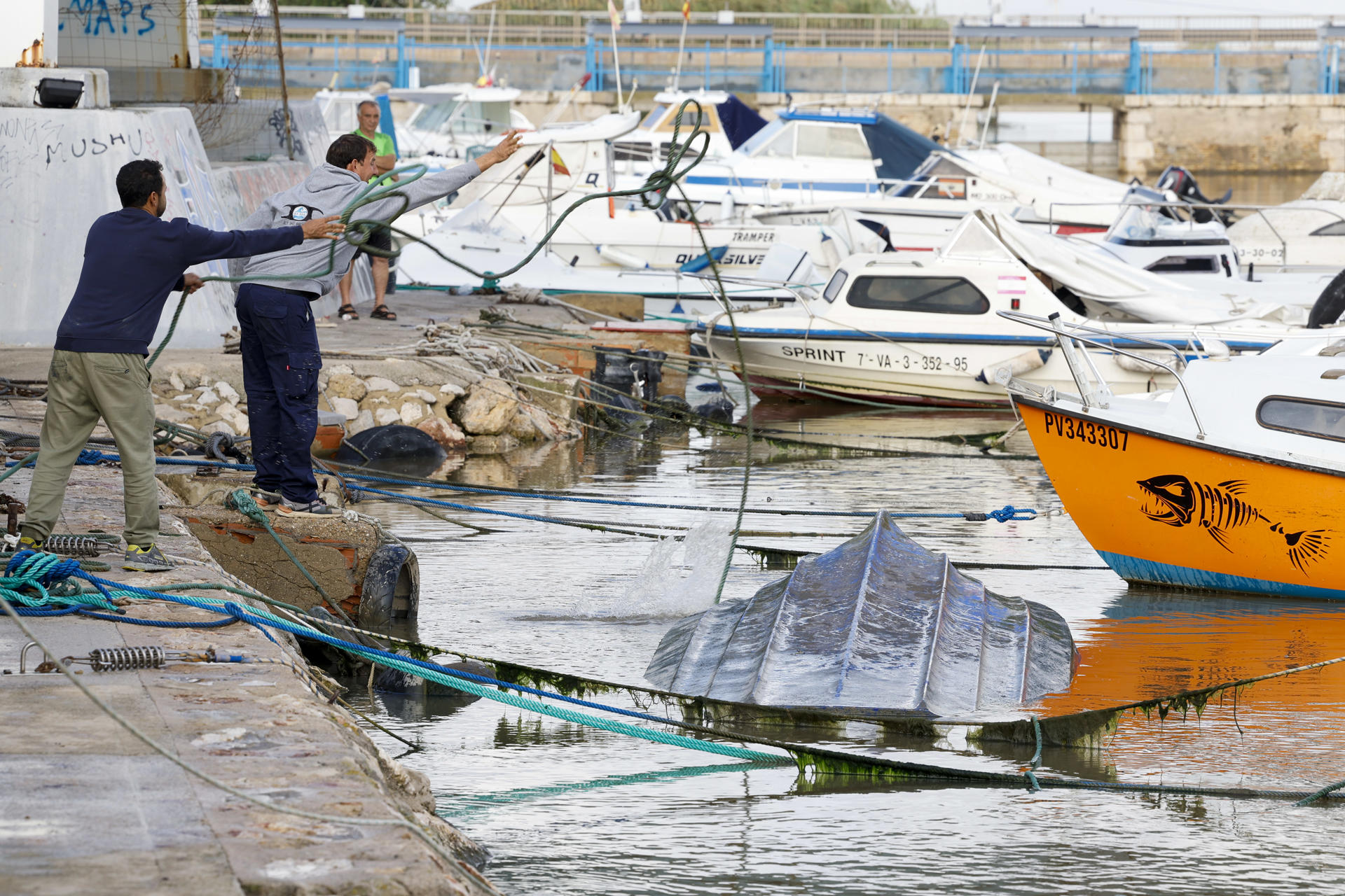 Varias personas intentan sacar uno de los barcos hundidos a causa del temporal de lluvia, este martes en Perelló (Sueca). EFE/ Ana Escobar