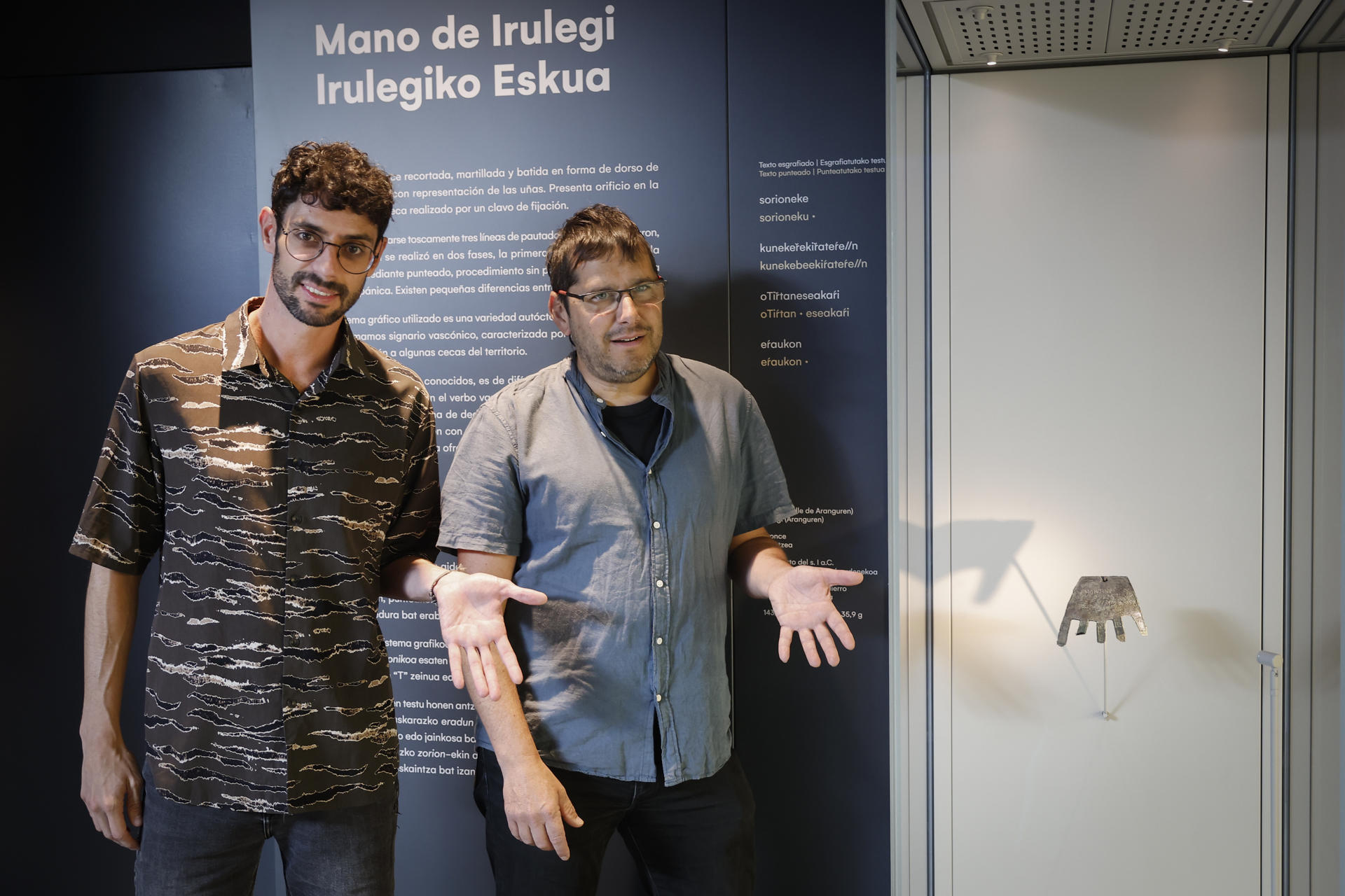 Los cineastas Iban Toledo (d) y Oroitz Zabala posan junto a la Mano de Irulegi en el Museo de Navarra tras haber filmado durante este verano en las excavaciones que se llevan a cabo en el Valle de Aranguren (Navarra) el rodaje de una película documental sobre esta pieza de bronce del siglo I a.c. hallada el 18 de junio de 2021 que indaga en el misterio del origen del euskera, quizás la lengua viva más antigua de Europa. EFE/ Villar López