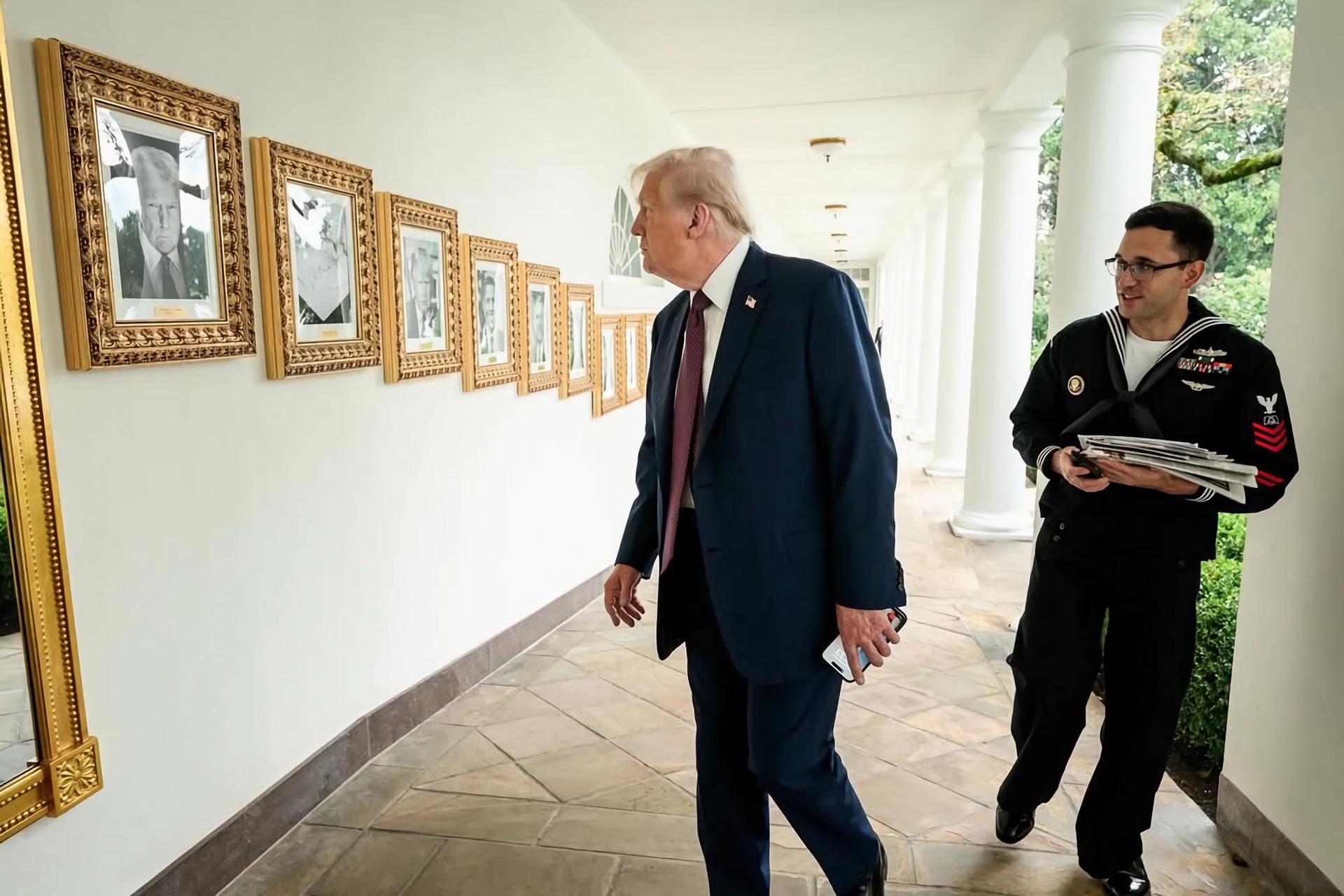 Fotografía divulgada este miércoles, 23 de septiembre, por la Casa Blanca donde se muestra al presidente estadounidense, Donald Trump (c), al mirar su foto durante la instalación de la galería de los 47 presidentes estadounidenses, ubicada en el pasillo de columnas que lleva al Despacho Oval de la sede del Ejecutivo estadounidense, en Washington (EE.UU.). EFE/Casa Blanca
