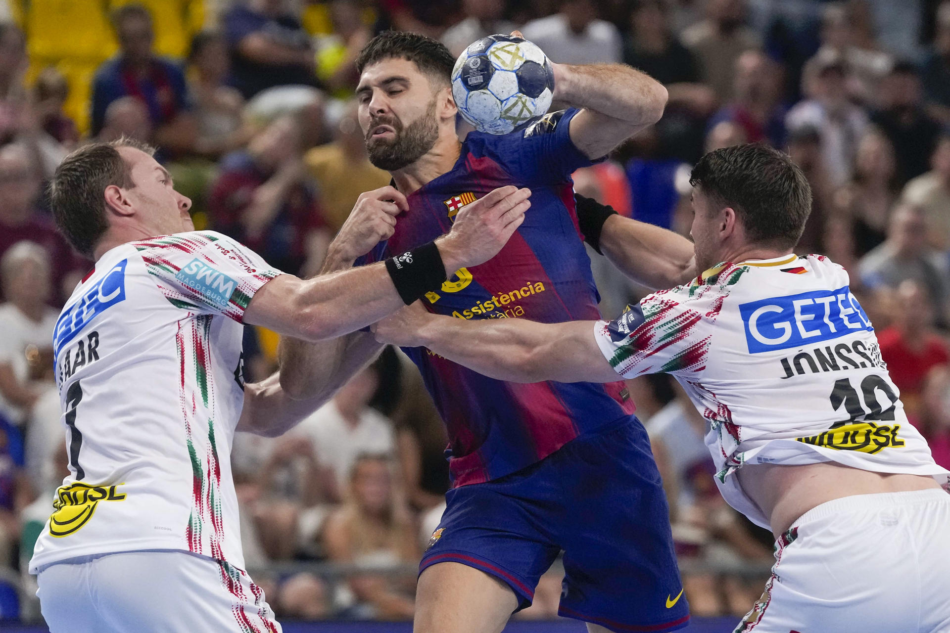 El extremo esloveno del Barça Janc Blaz (c) lucha con Claar (i) y Jonsson (d), del Magdeburgo alemán, durante el partido correspondiente a la segunda jornada de la fase regular de la Liga de Campeones de Balonmano este jueves en el Palau Blaugrana. EFE/Enric Fontcuberta

