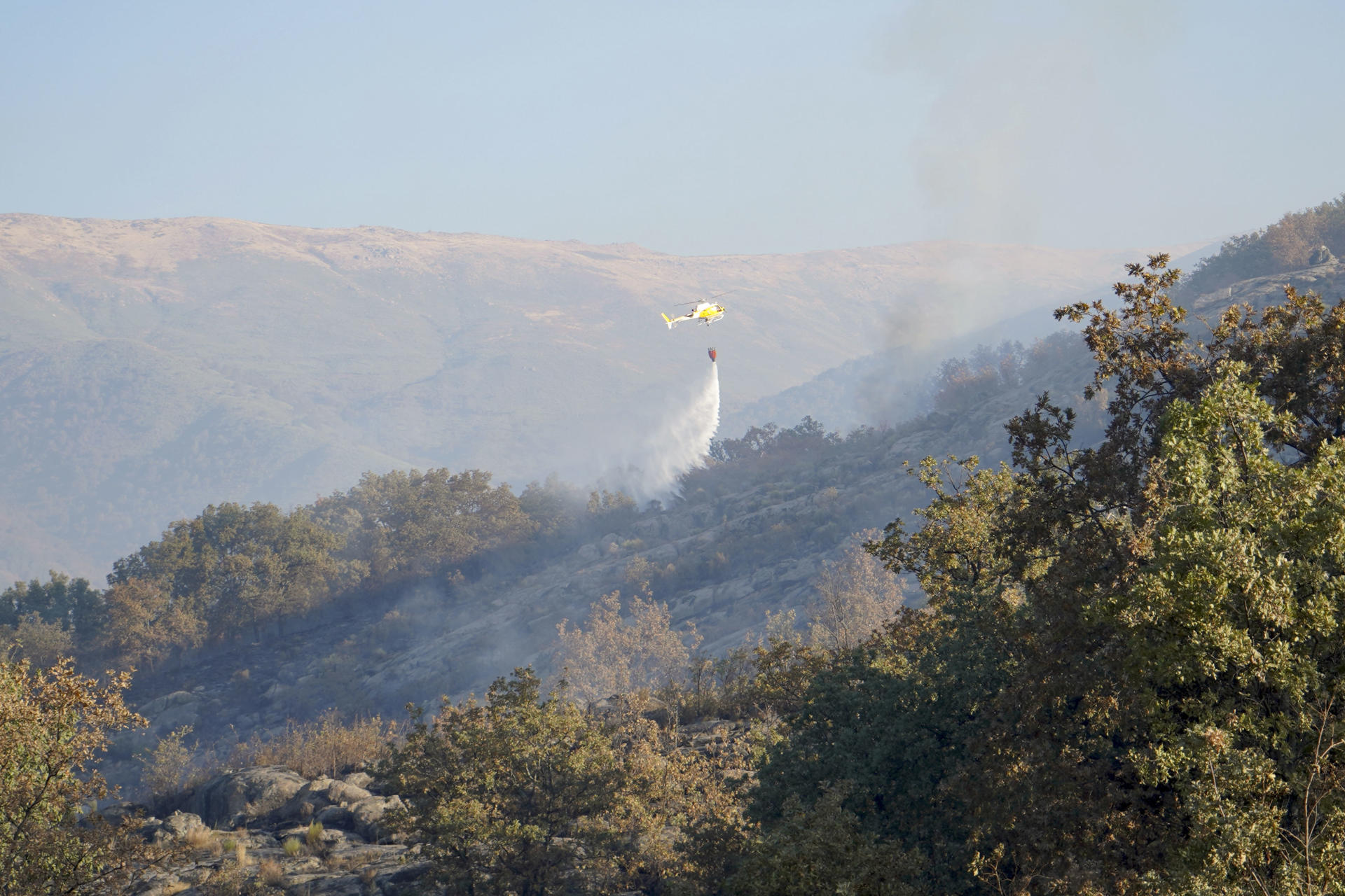 Un helicóptero trabaja en las labores de extinción del incendio forestal declarado este domingo en Cuacos de Yuste (Cáceres), que ha arrasado 438 hectáreas de matorral y arbolado. EFE/  EDUARDO PALOMO