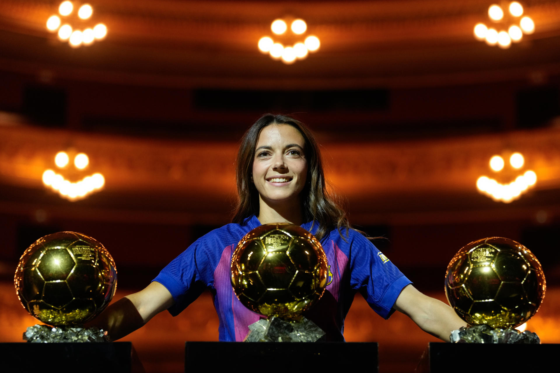 La centrocampista del FC Barcelona, Aitana Bonmatí, reciente ganadora del 'Balón de oro', el tercero consecutivo en su carrera, posa con los tres trofeos en una sesión fotográfica en el Gran Teatre del Liceu barcelonés.EFE/ Enric Fontcuberta