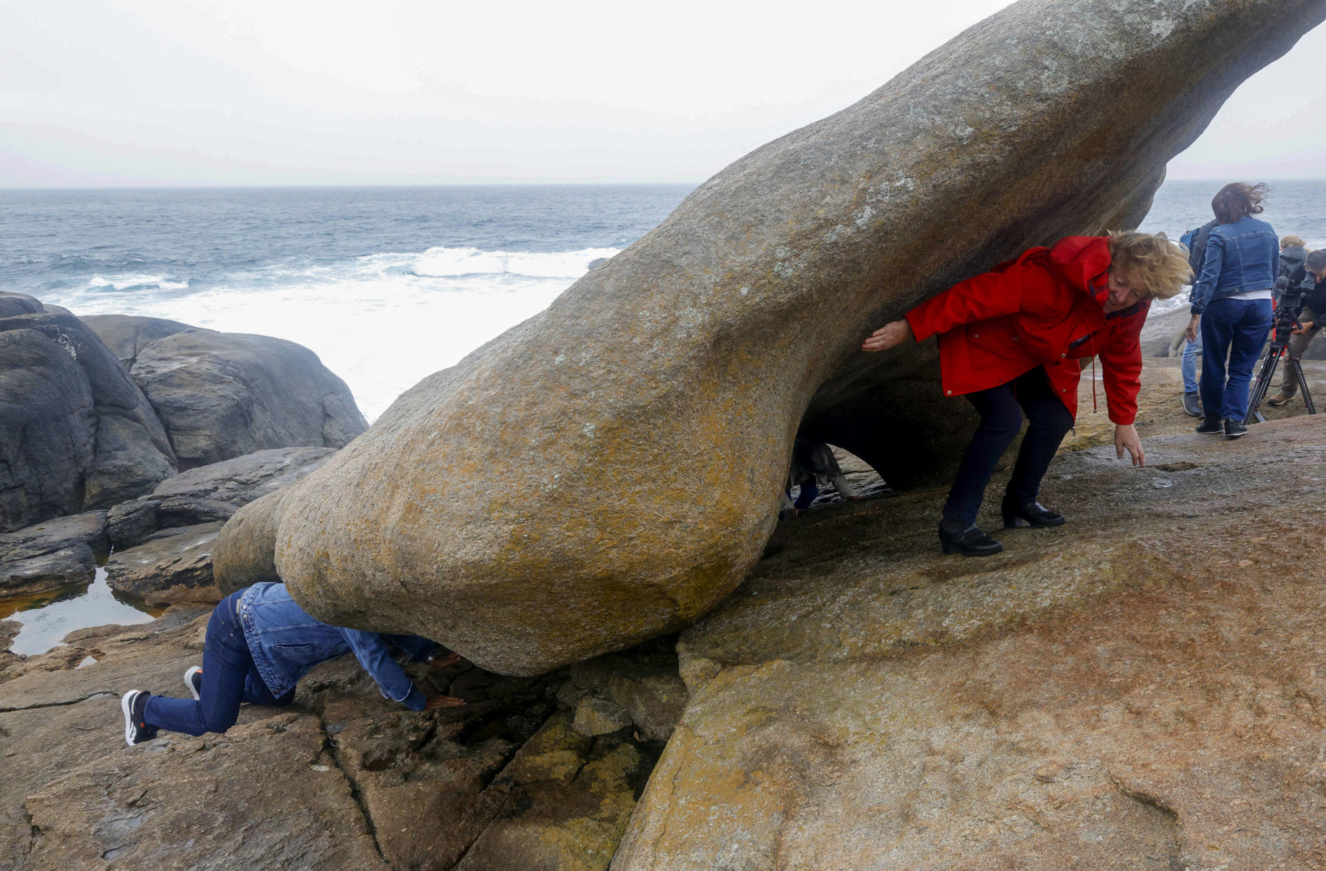 Fieles pasa bajo la Pedra dos Cadrís tal y como manda la tradición durante la romería de la Virxe da Barca, que este 2025 ha captado el interés de medios internacionales, este domingo en Muxia. EFE/Kiko Delgado