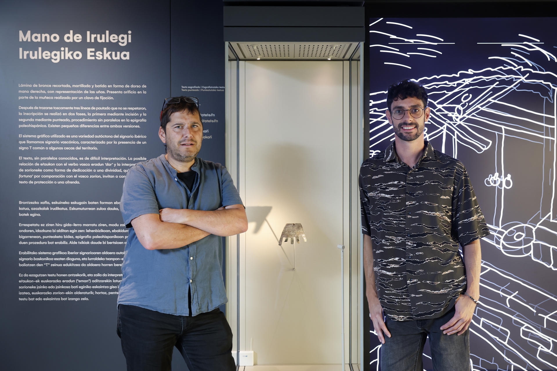 Los cineastas Iban Toledo (i) y Oroitz Zabala posan junto a la Mano de Irulegi en el Museo de Navarra tras haber filmado durante este verano en las excavaciones que se llevan a cabo en el Valle de Aranguren (Navarra) el rodaje de una película documental sobre esta pieza de bronce del siglo I a.c. hallada el 18 de junio de 2021 que indaga en el misterio del origen del euskera, quizás la lengua viva más antigua de Europa. EFE/ Villar López