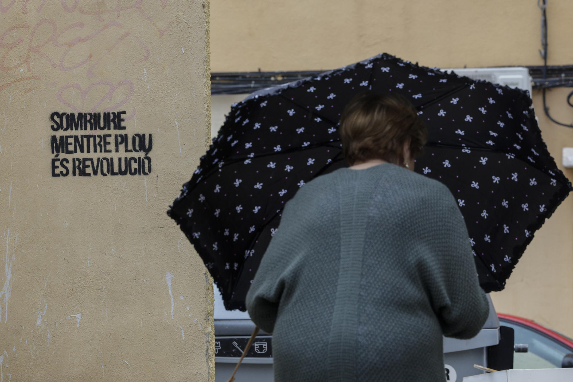 Una mujer se protegía el lunes de la lluvia con un paraguas junto a una pintada con el lema "Sonreír mientras llueve es revolución", en Burjassot (Valencia). EFE/Kai Försterling