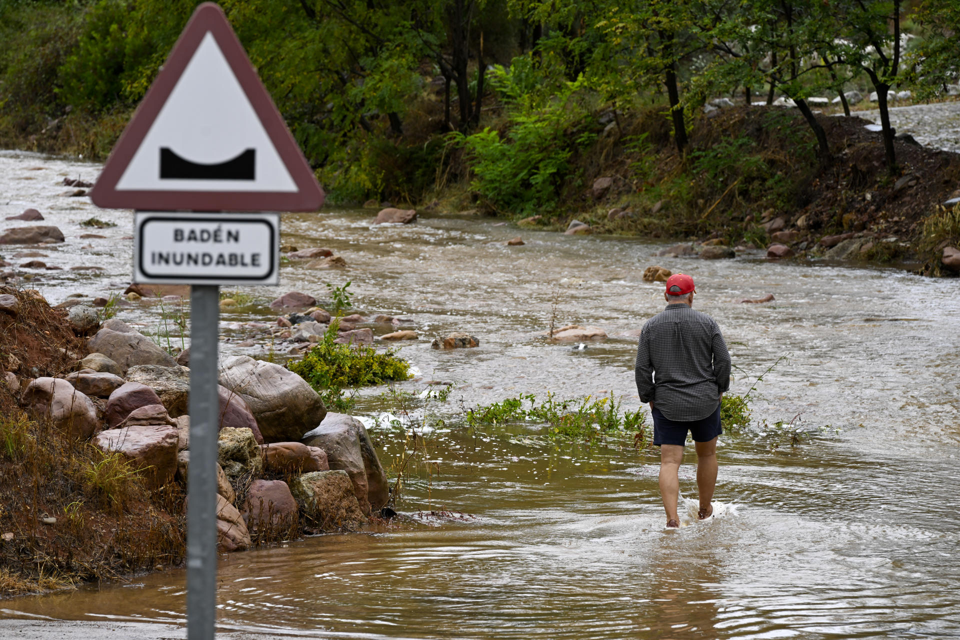 Un hombre cruza un badén inundable durante este lunes en el que el aviso rojo (riesgo extremo) por precipitaciones que pueden acumular 180 litros por metro cuadrado en doce horas estará activo hasta la medianoche de hoy en el litoral de la provincia de Valencia, mientras que ha finalizado en el litoral norte de Castellón este mediodía. EFE/Andreu Esteban