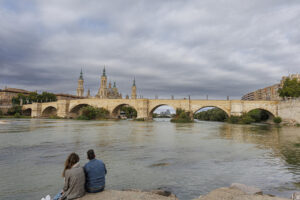 Dos personas observan el paso del rio Ebro por Zaragoza este domingo cuando la Confederación Hidrográfica del Ebro (CHE), mantiene el aviso por posibles crecidas en barrancos y cauces menores por la previsión de tormentas en Navarra, Aragón, Cataluña y la Comunidad Valenciana. EFE/ Javier Belver
