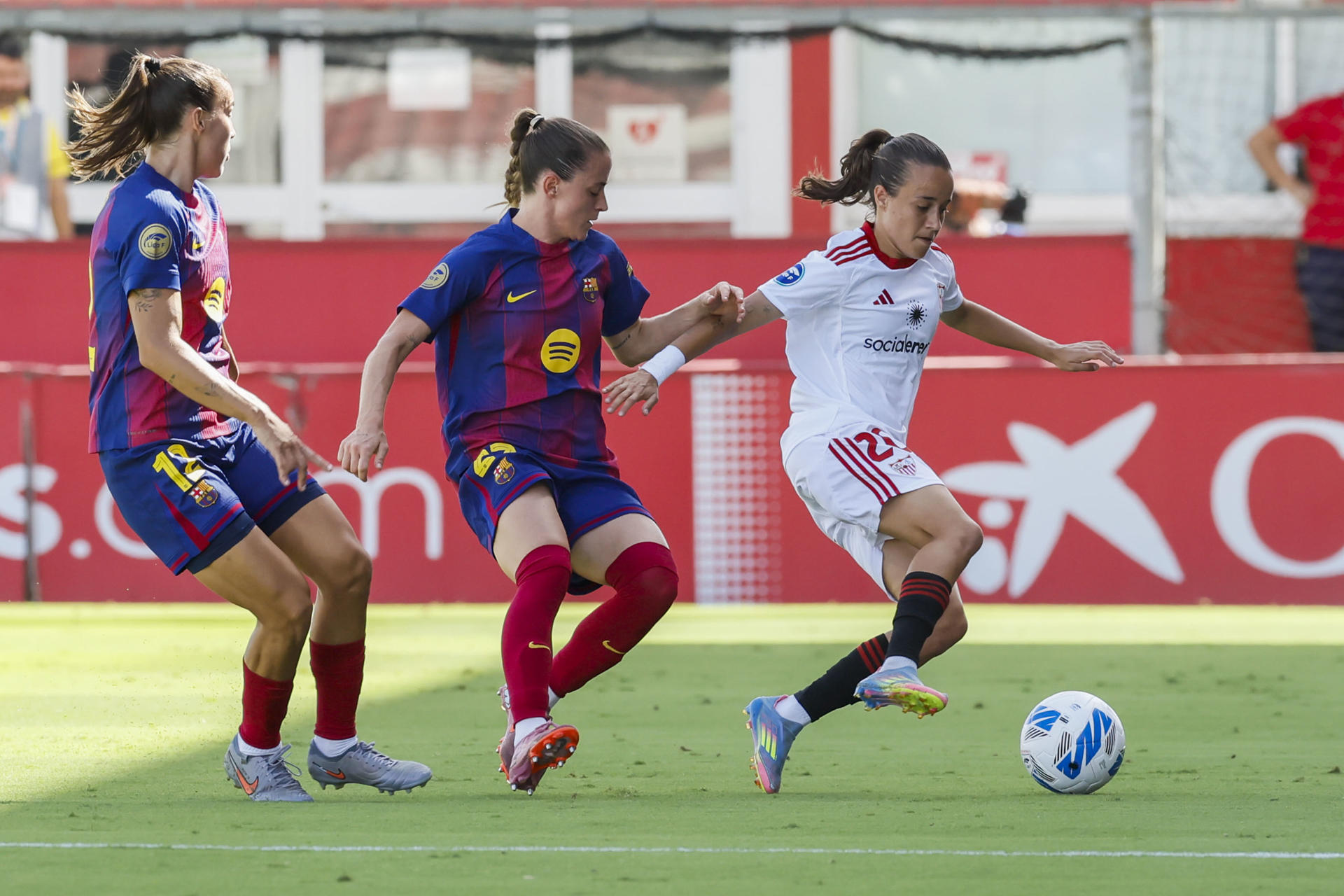 La centrocampista del Sevilla Rosa Márquez (d) pelea un balón ante la defensa del Barcelona Ona Batlle (c) durante el partido de la jornada 4 de la Liga F, entre el Barcelona y el Sevilla, que se celebra este domingo en la Ciudad Deportiva Jose Ramón Cisneros Palacios Sevilla Futbol Club en la capital andaluza. EFE/ Jose Manuel Vidal