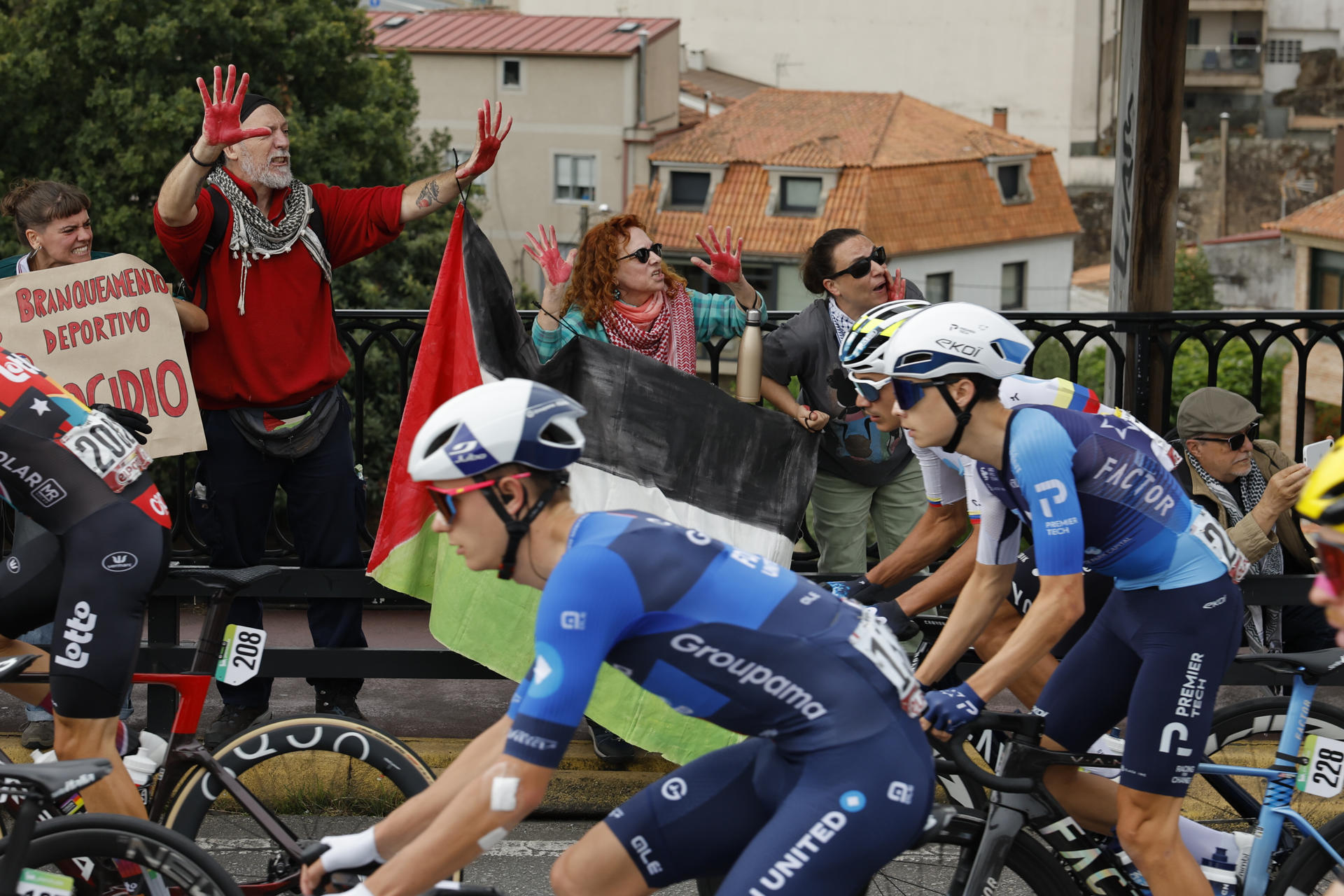 Los ciclistas del equipo Israel Premier Tech pasan ante las protestas propalestina durante la etapa 16 de la Vuelta Ciclista a España que se disputa este martes entre Poio y Mos-Castro de Herville (Pontevedra), de 167.9 km de recorrido. EFE/ Lavandeira Jr