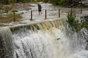 Un hombre cruza un badén inundable durante este lunes en el que el aviso rojo (riesgo extremo) por precipitaciones que pueden acumular 180 litros por metro cuadrado en doce horas estará activo hasta la medianoche de hoy en el litoral de la provincia de Valencia, mientras que ha finalizado en el litoral norte de Castellón este mediodía. EFE/Andreu Esteban