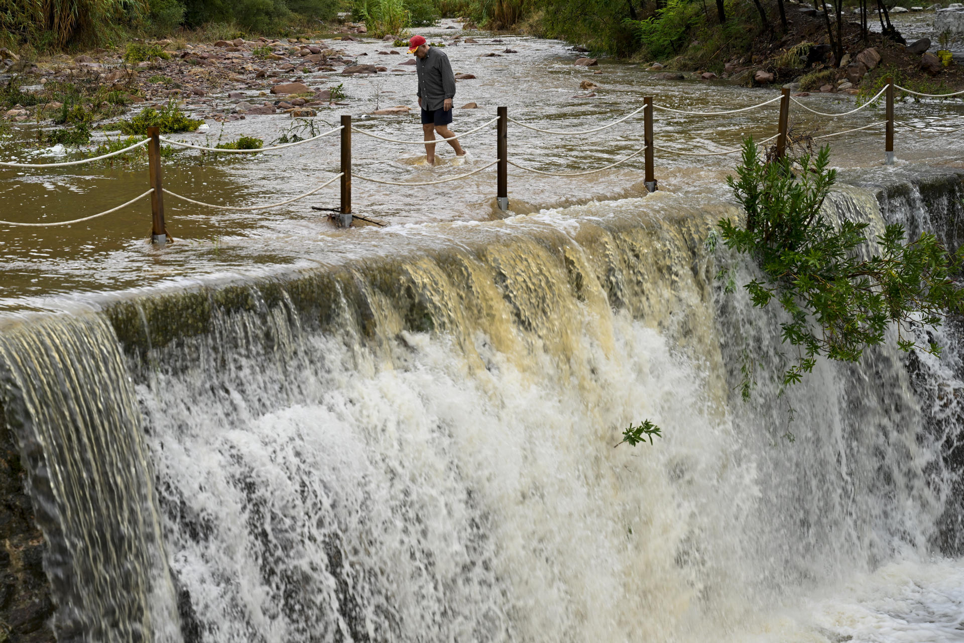 Un hombre cruza un badén inundable durante este lunes en el que el aviso rojo (riesgo extremo) por precipitaciones que pueden acumular 180 litros por metro cuadrado en doce horas estará activo hasta la medianoche de hoy en el litoral de la provincia de Valencia, mientras que ha finalizado en el litoral norte de Castellón este mediodía. EFE/Andreu Esteban