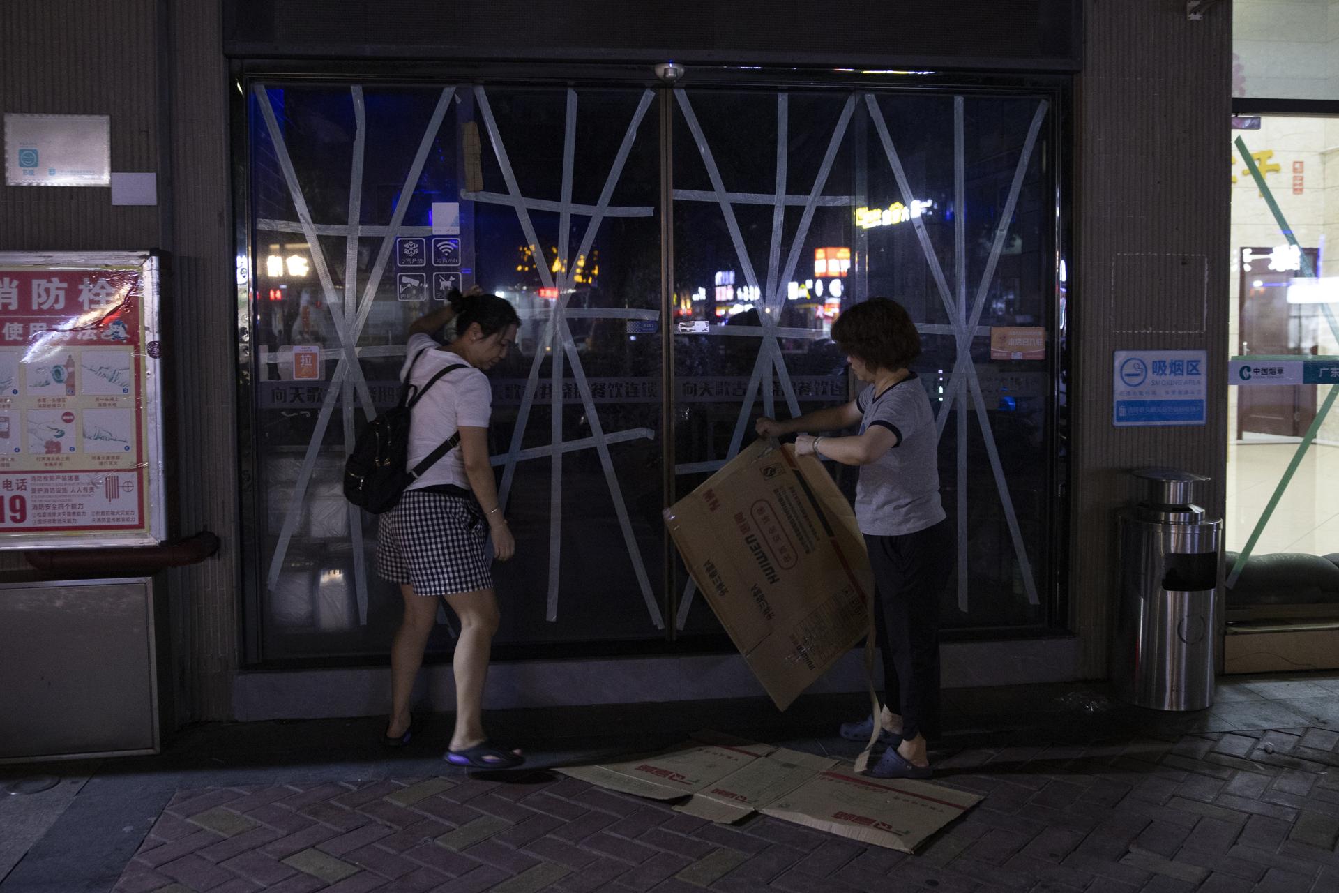Dos mujeres usan pedazos de cartón para proteger las puertas de vidrio selladas con cinta adhesiva de un restaurante, como parte de los preparativos ante la llegada del tifón Ragasa, en Yangjiang, provincia de Cantón (Guangdong). EFEANDRES MARTINEZ CASARES