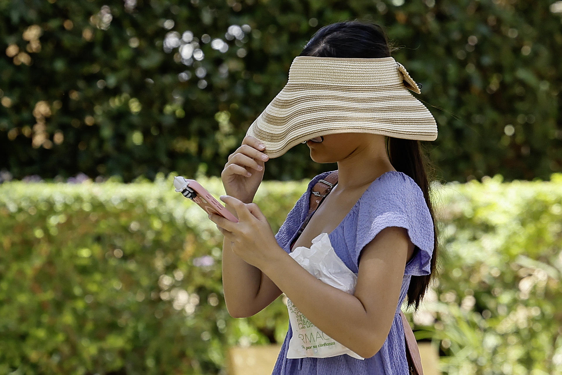Una mujer se tapa con un sombrero la cara para resguardarse del sol mientras camina por un parque en Sevilla en una imagen de archivo. EFE /José Manuel Vidal