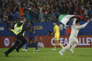 Seguridad persigue a un espontaneo con una bandera de Palestina durante el partido de la jornada 5 de LaLiga que FC Barcelona y Getafe CF disputaron en el Estadi Johan Cruyff. EFE/ Andreu Dalmau