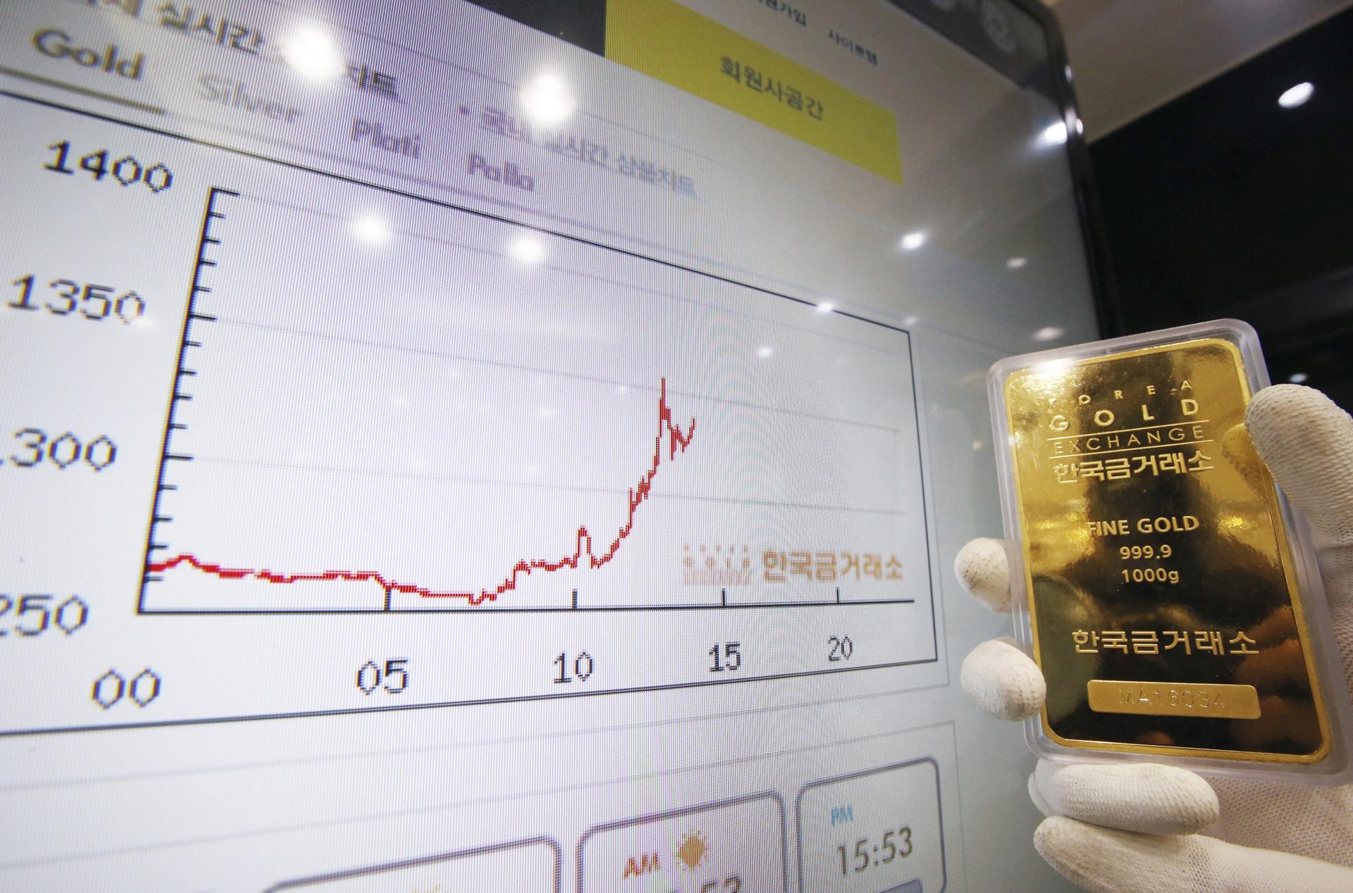 Imagen de archivo de un trabajador del Korea Gold Exchange (KGE) mostrando un lingote de oro junto a una pantalla que muestra la evolución del precio del metal. EFE/Yonhap